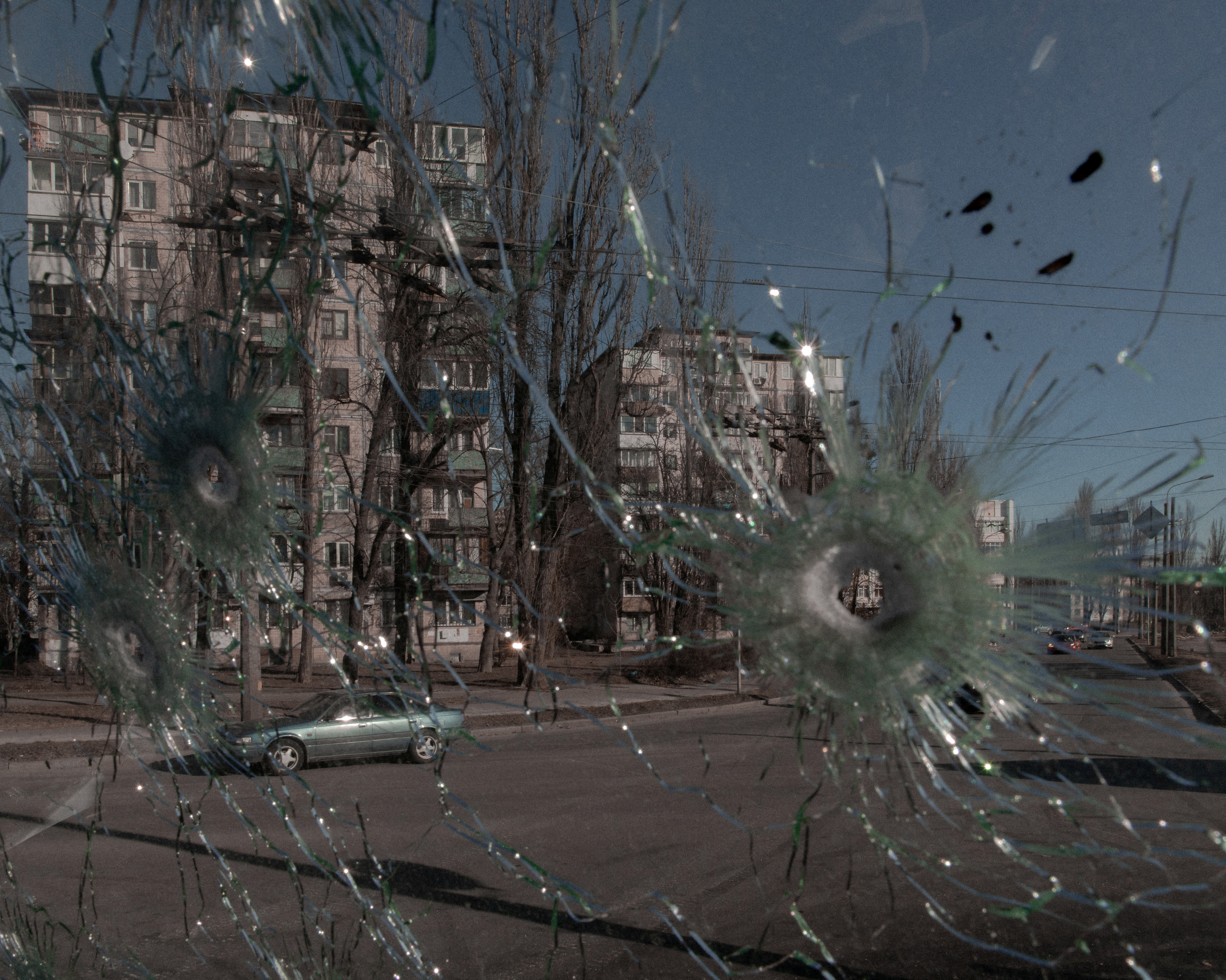 Cars are seen through the damaged window of a vehicle hit by bullets in Kyiv