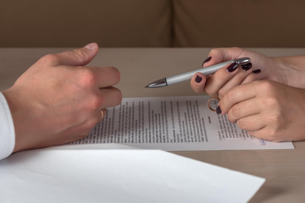 Wife and husband signing divorce documents, woman returning wedding ring