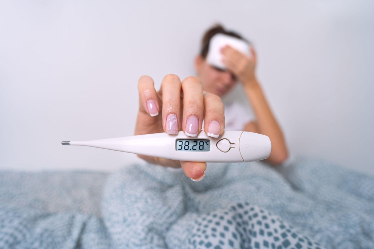 Sick woman with a high fever showing medical thermometer with temperature 38,2. Woman measuring body temperature