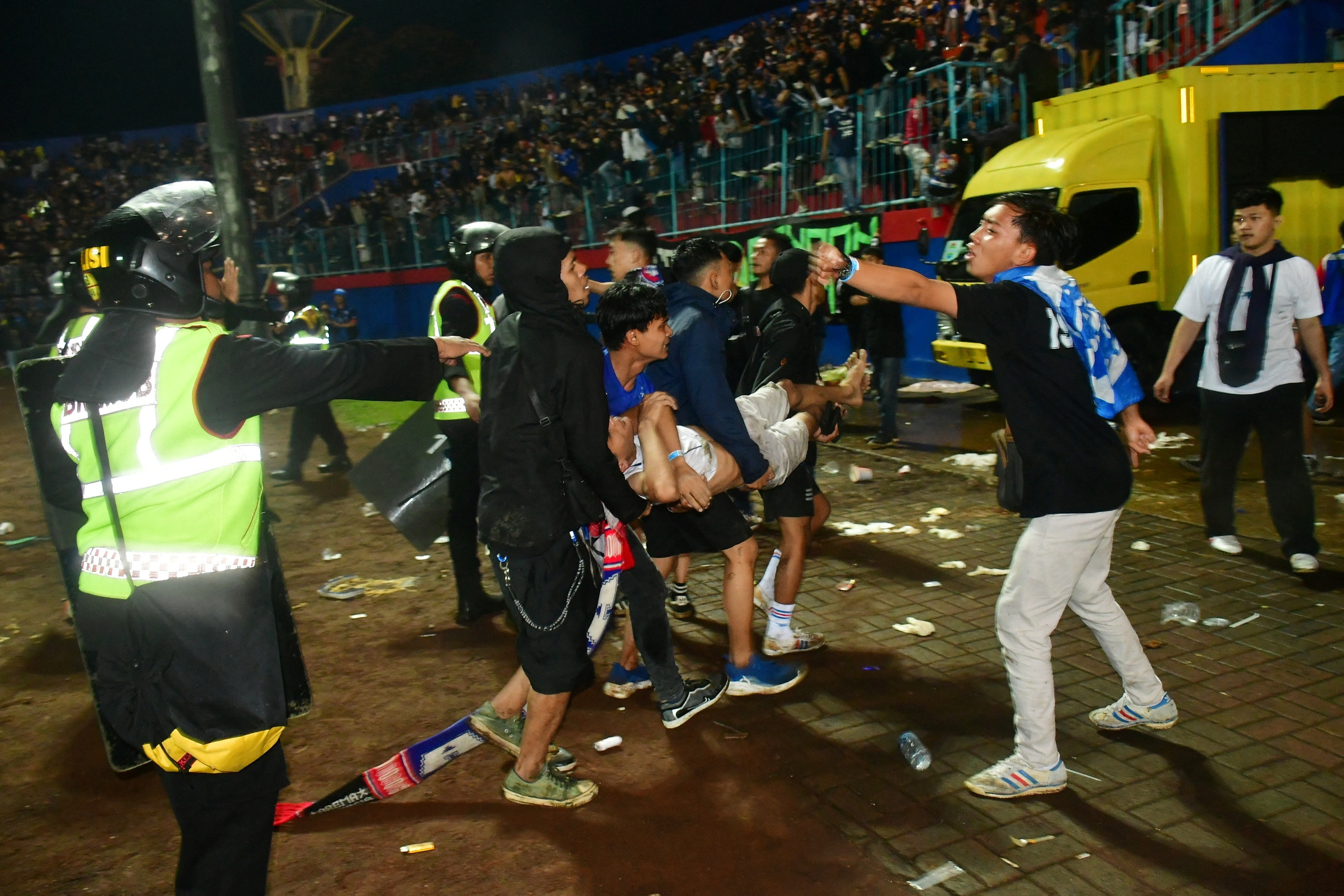 Supporters evacuate a man due to tear gas fired by police during the riot after the football match between Arema vs Persebaya at Kanjuruhan Stadium