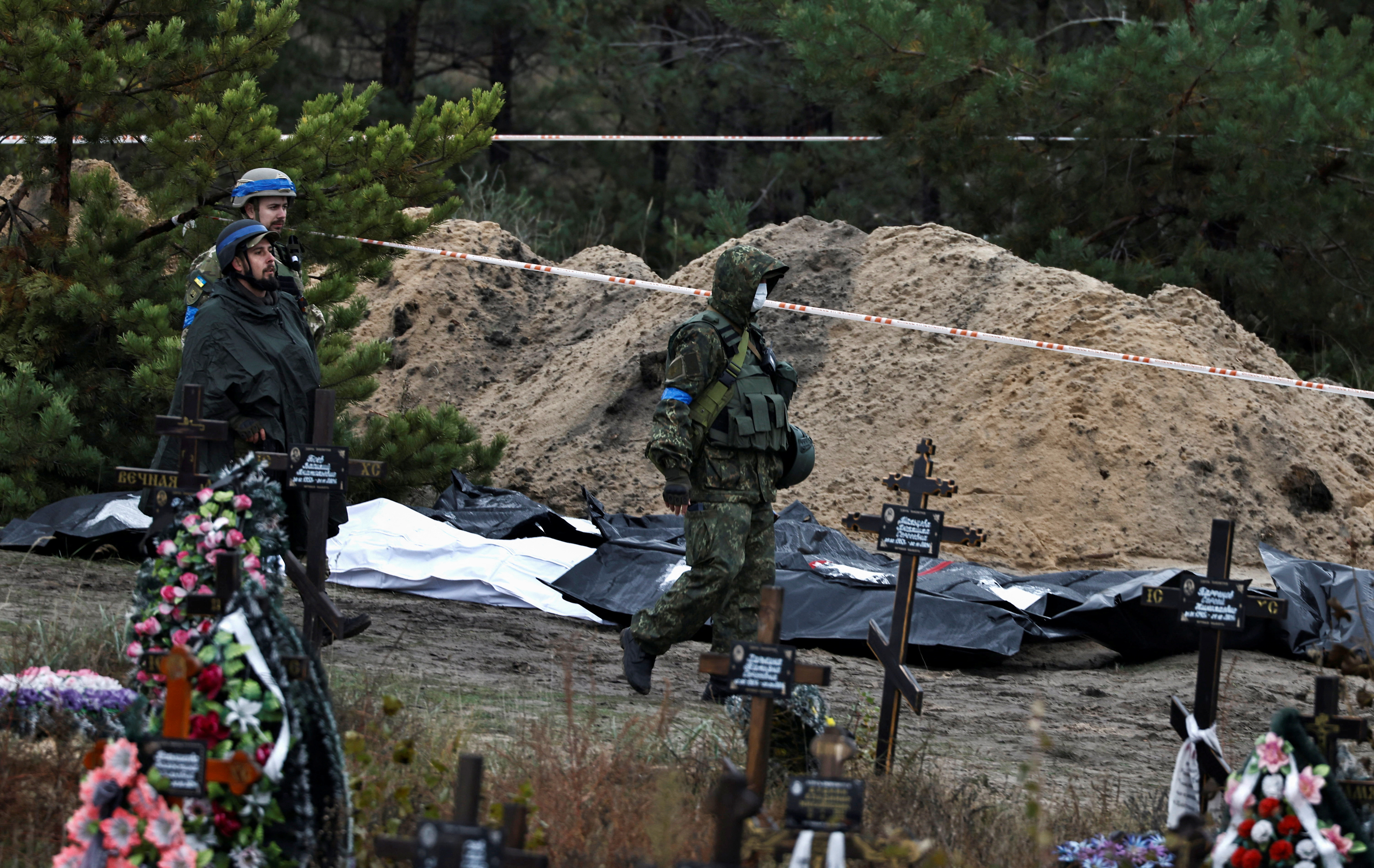 Army officers walk past bodies  exhumed from, what Ukrainians said, a mass grave, in the newly recaptured town of Lyman