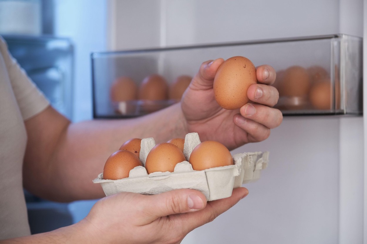 Close up of a man placing eggs in the fridge door shelf.