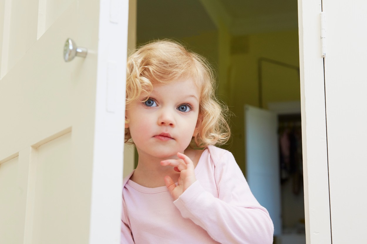 Female toddler peering from door