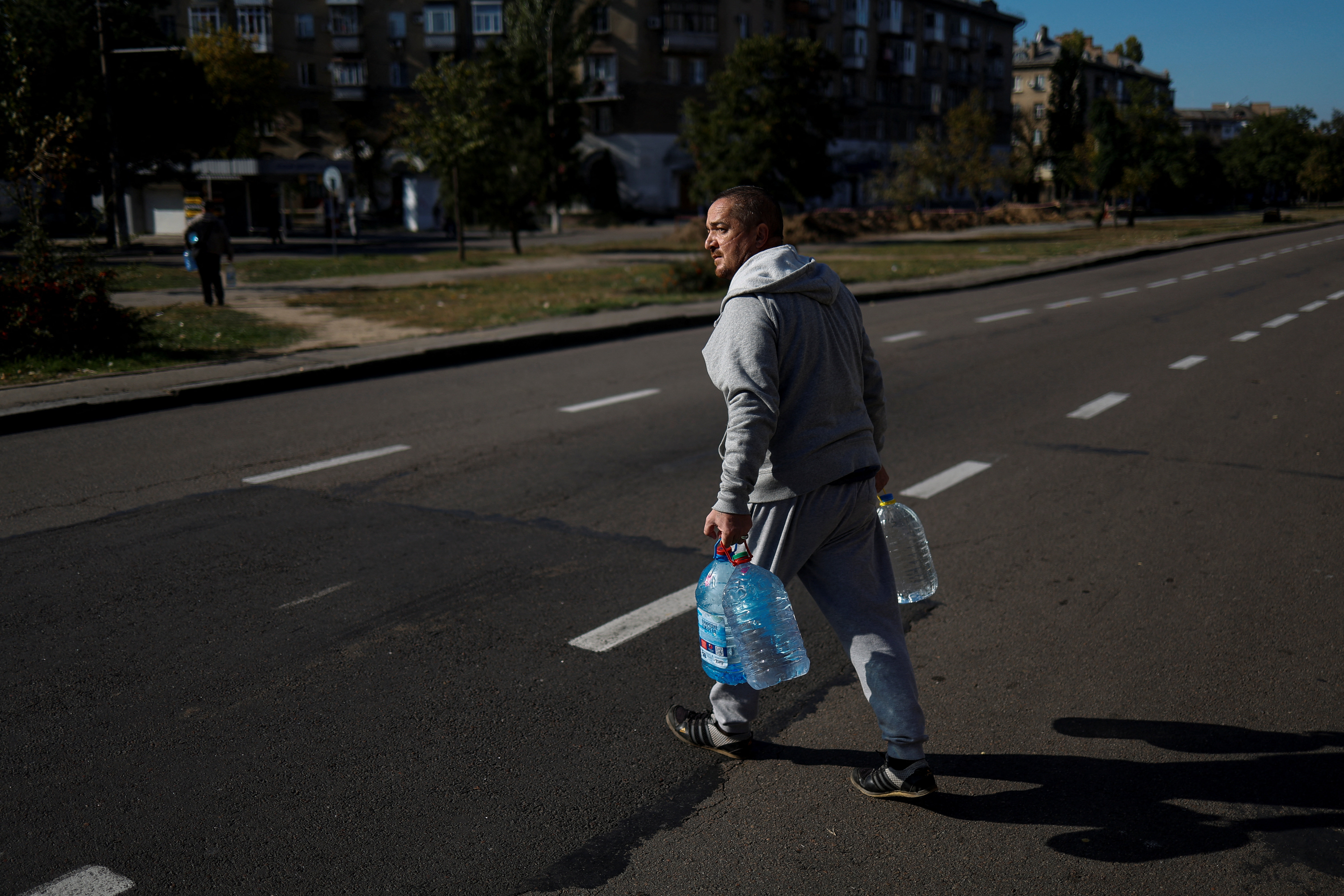 Local man crosses a street with bottles of fresh drinking water in Mykolaiv