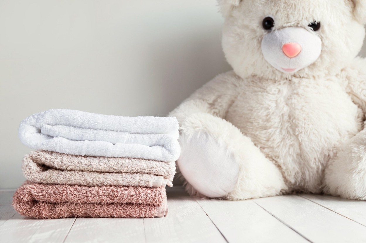 Stack of spa towels on white wooden table with white soft toy bear on background. Childrens washing concept.