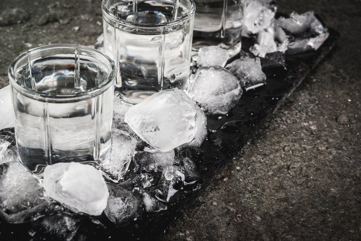 Alcohol and cocktails. Three glasses of vodka on a slate tray, with ice. On a black stone table, Copy space