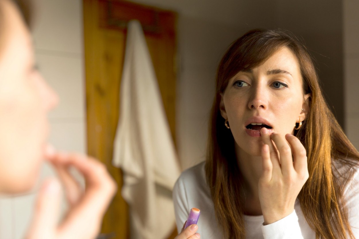 Lips care. Woman applying balsam on lips in bathroom
