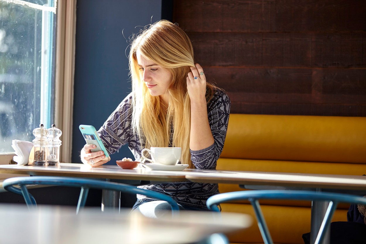 Young woman alone in cafe reading smartphone texts