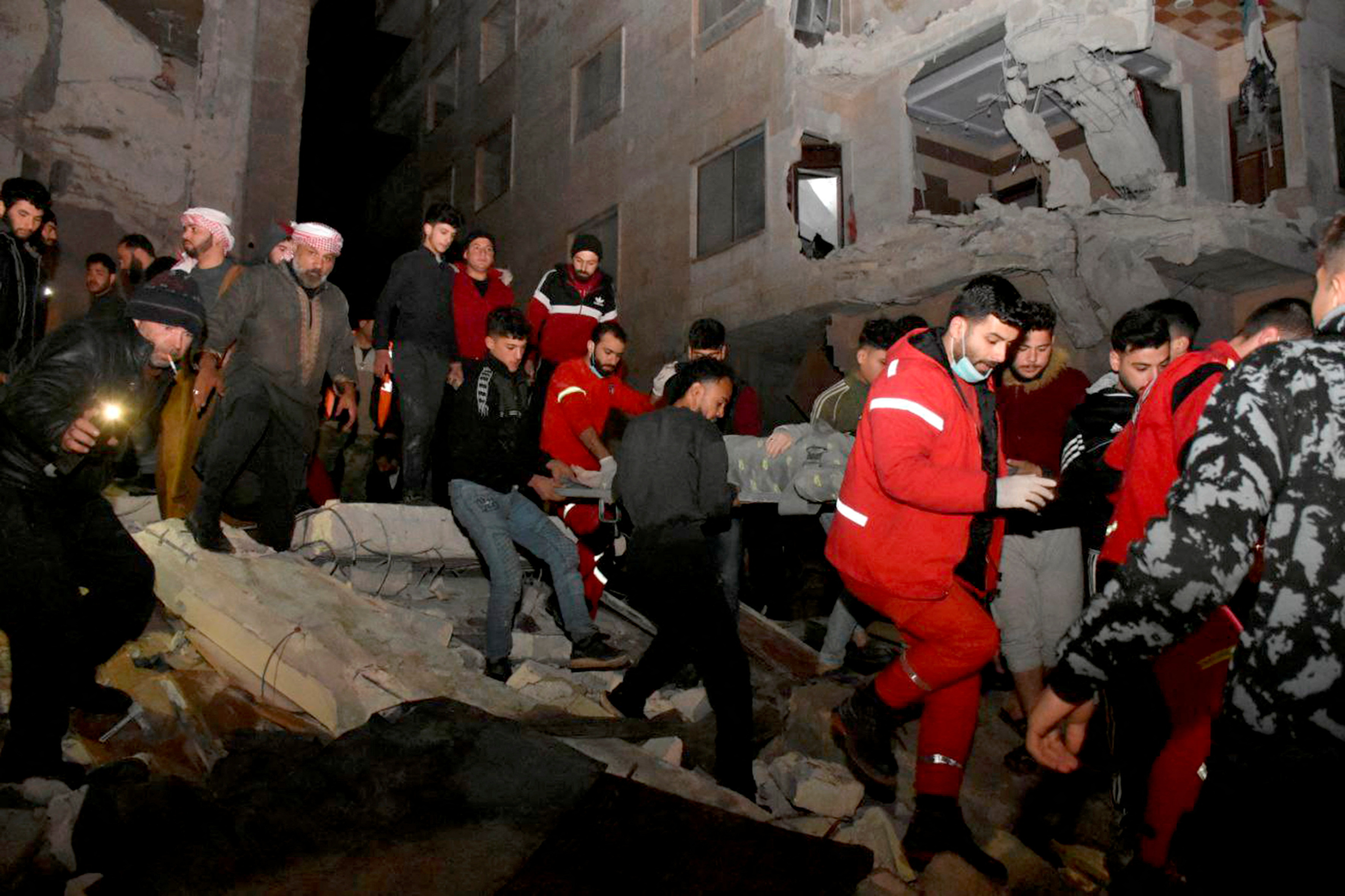 Rescuers carry a person on a stretcher at the site of a collapsed building, following an earthquake, in Hama