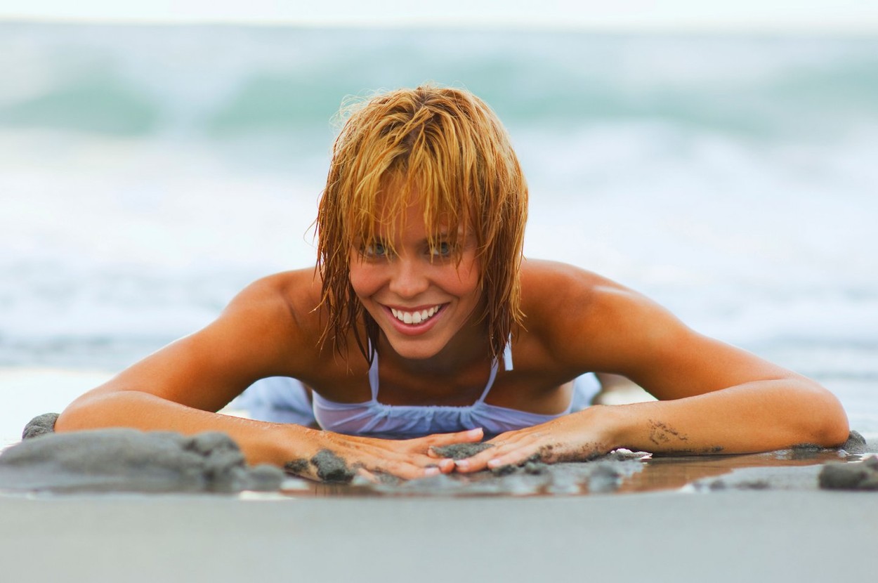 Young energetic woman in bikini lying at the beach in sudsy seawater.