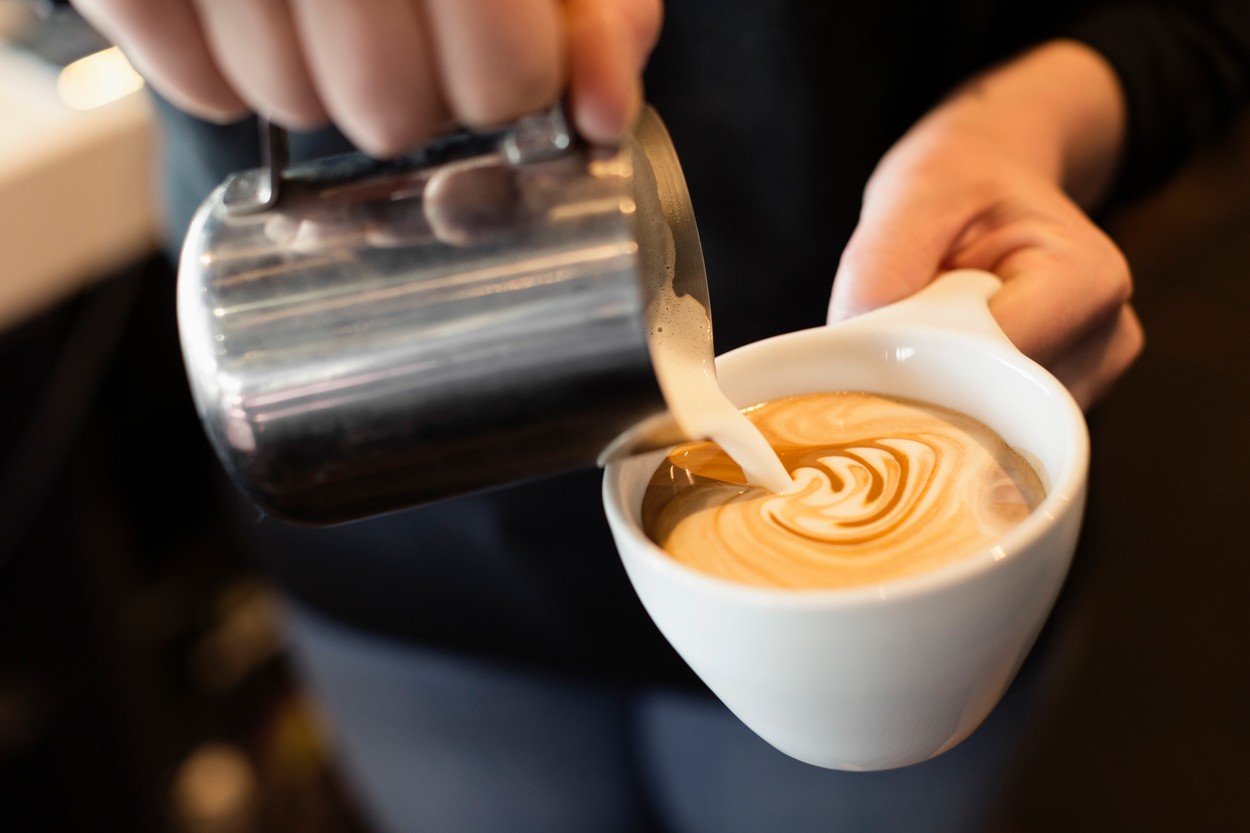 Coffee shop barista pouring milk into coffee, mid section, close-up
