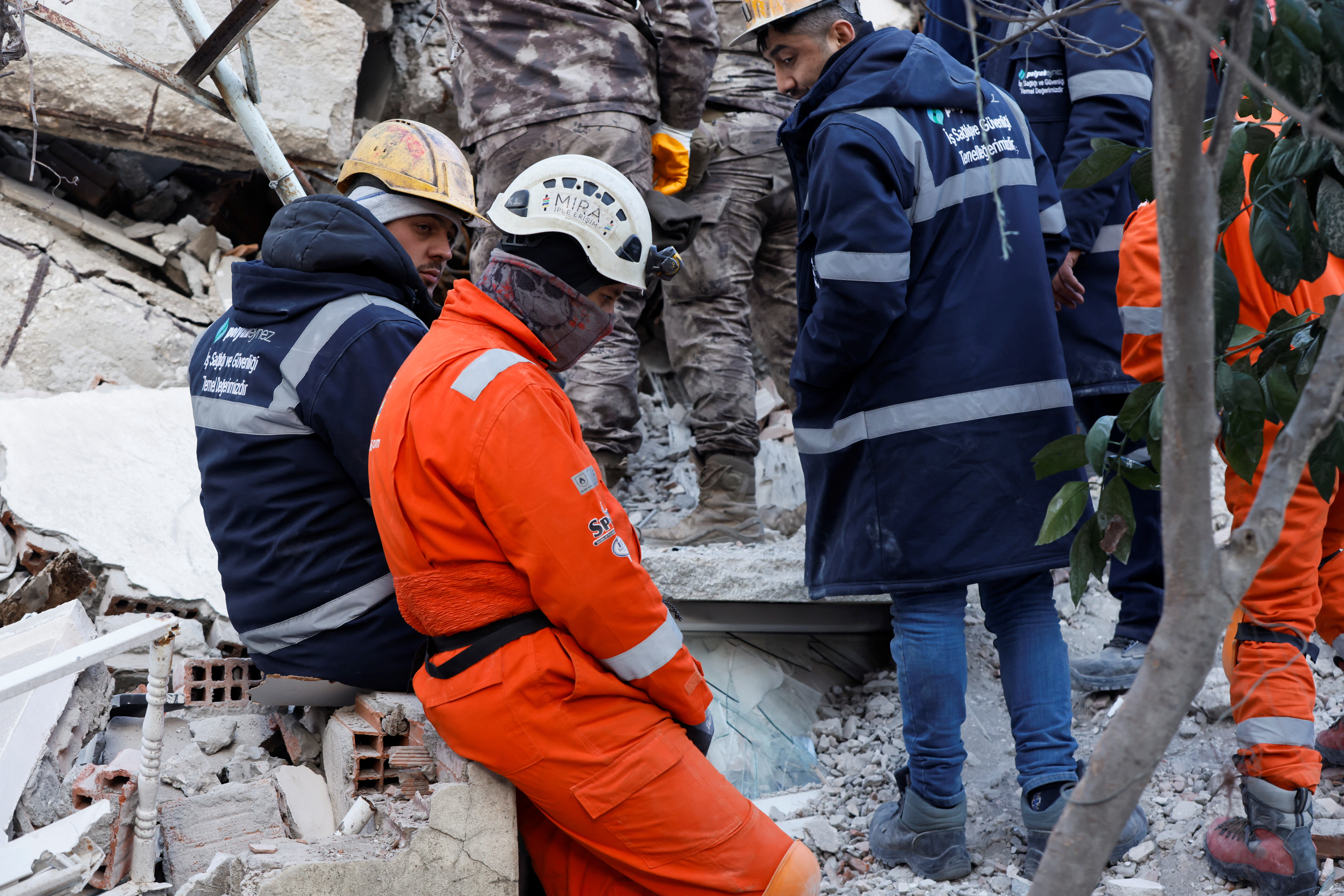 Young rescuers sit surrounded by rubble in the aftermath of the deadly earthquake in Hatay