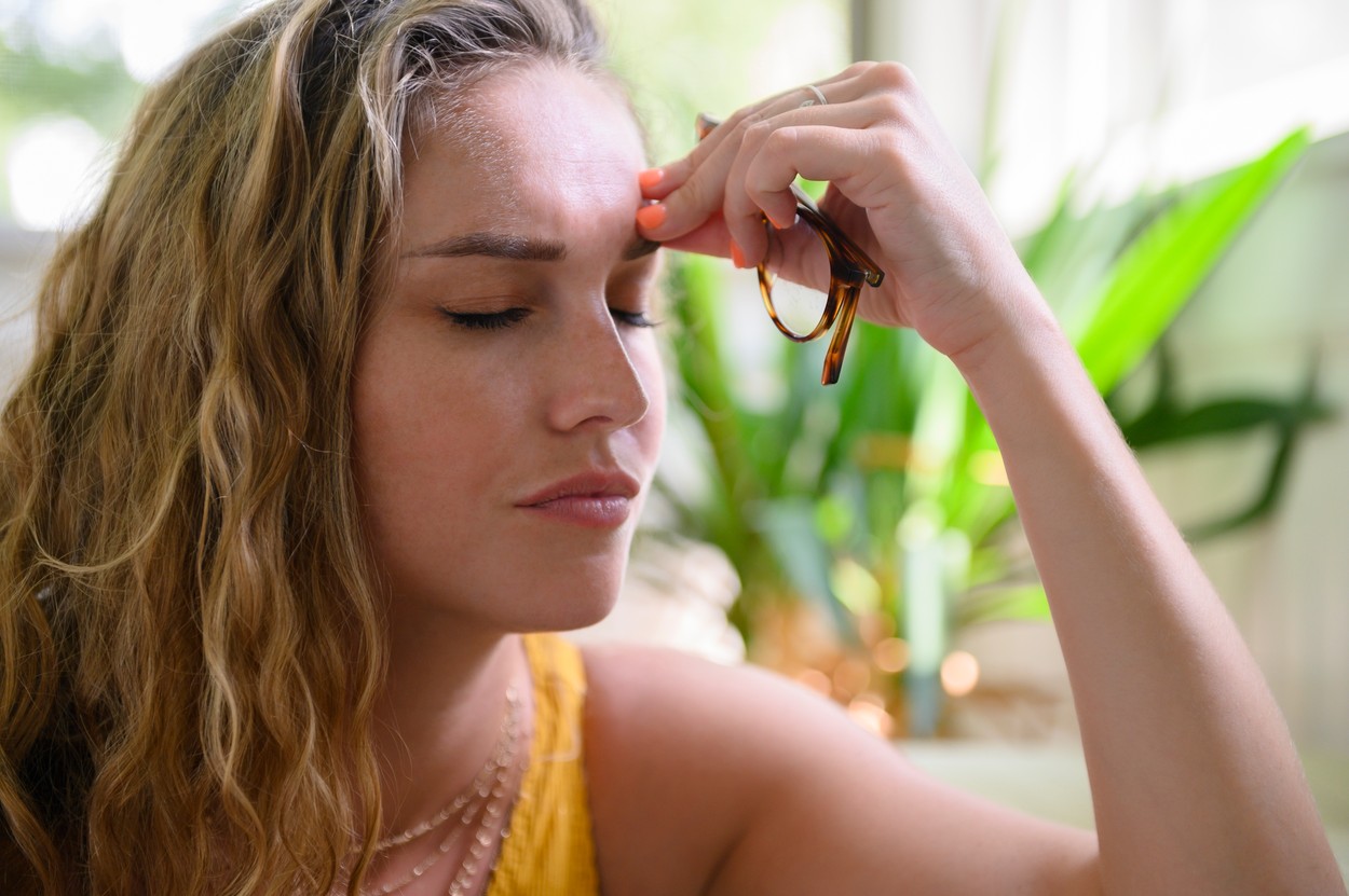 Young woman with headache holding glasses
