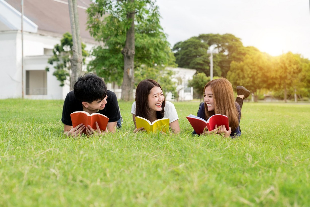 Group of friends studying outdoors in park at school. Three Asian high school student lying in grass at school.