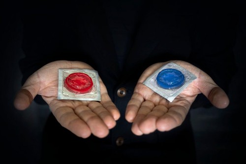 The concept of choice. A red and blue condom in a man's hand on a dark background. Safe sex.