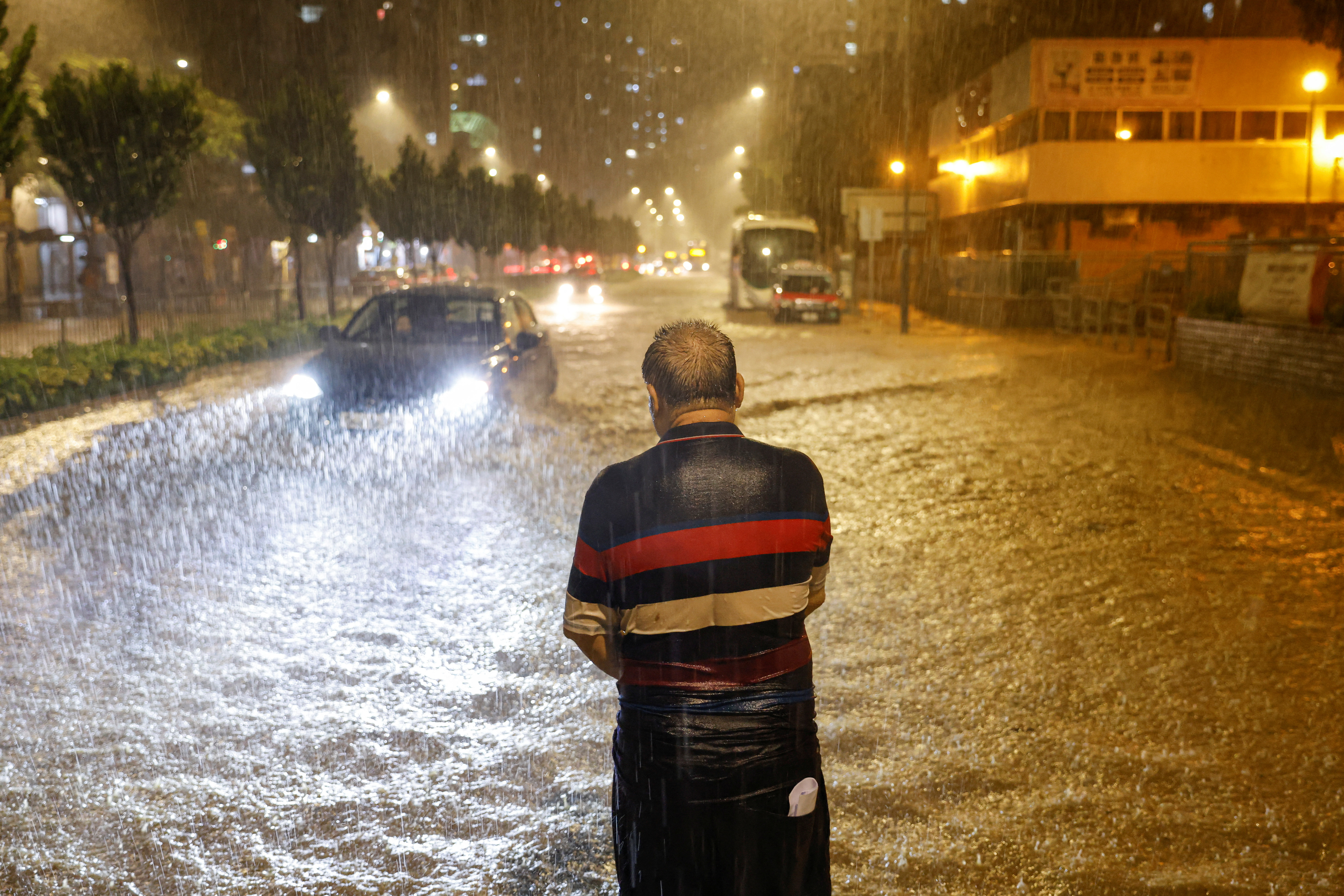 A man stands in the middle of a flooded road, attempting to get the attention of the bus driver during heavy rain, in Hong Kong