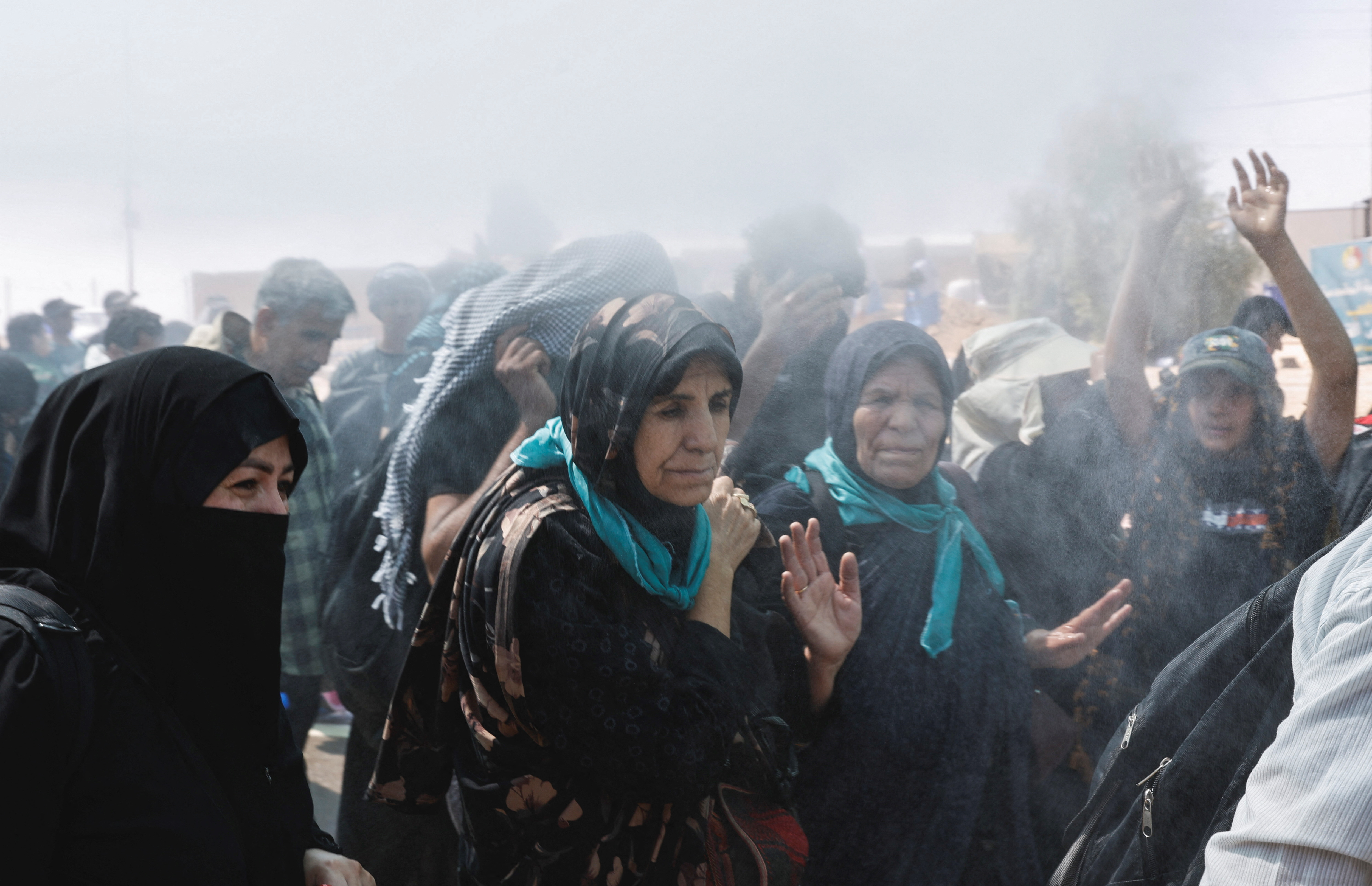 Iranian Shi'ite pilgrims walk on a road and cool off under water sprinklers, amid high temperatures, in Zurbatia