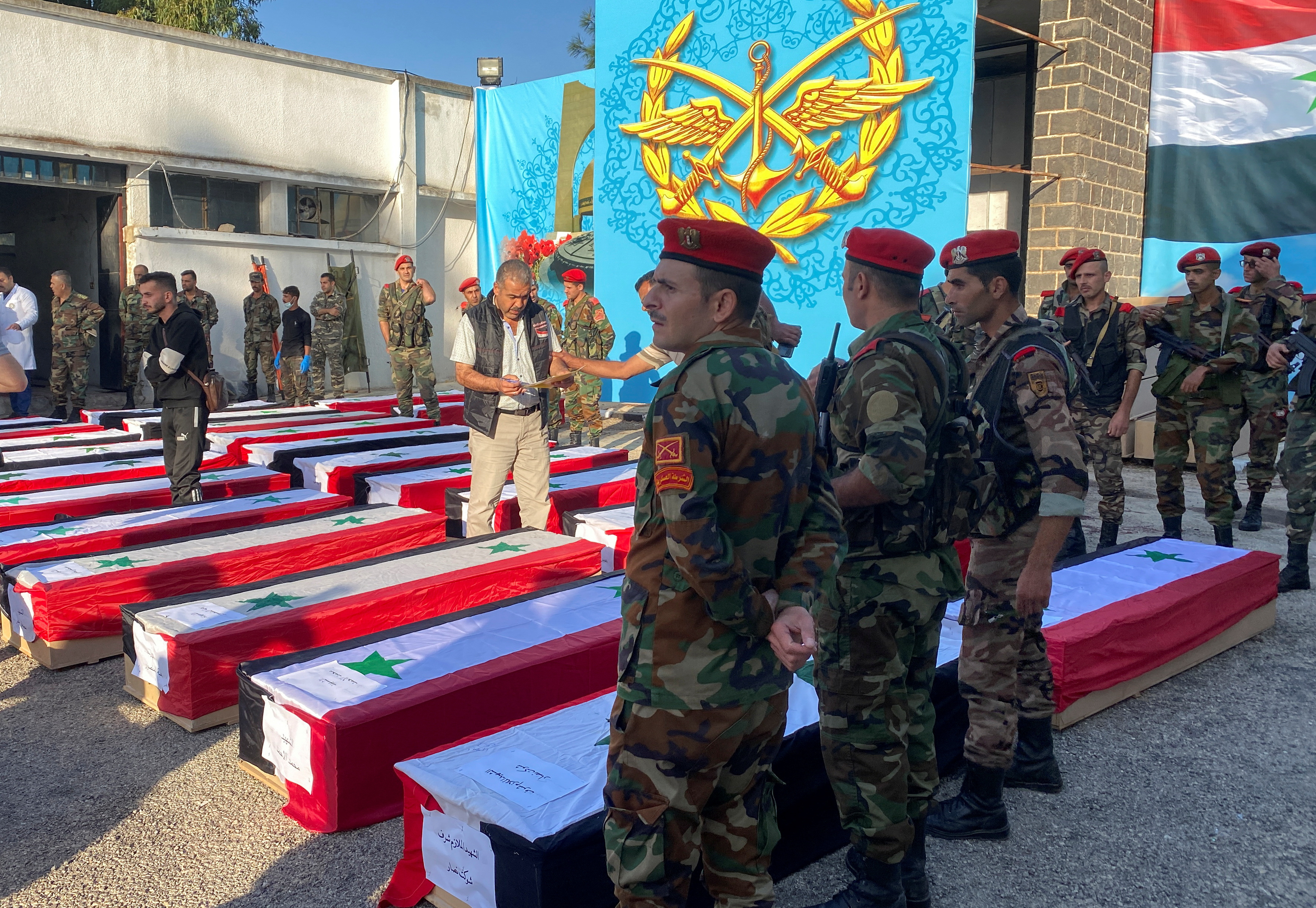 Military police stand near coffins with the bodies of some of the people who were killed in a drone attack on a military academy, outside a military hospital in Homs