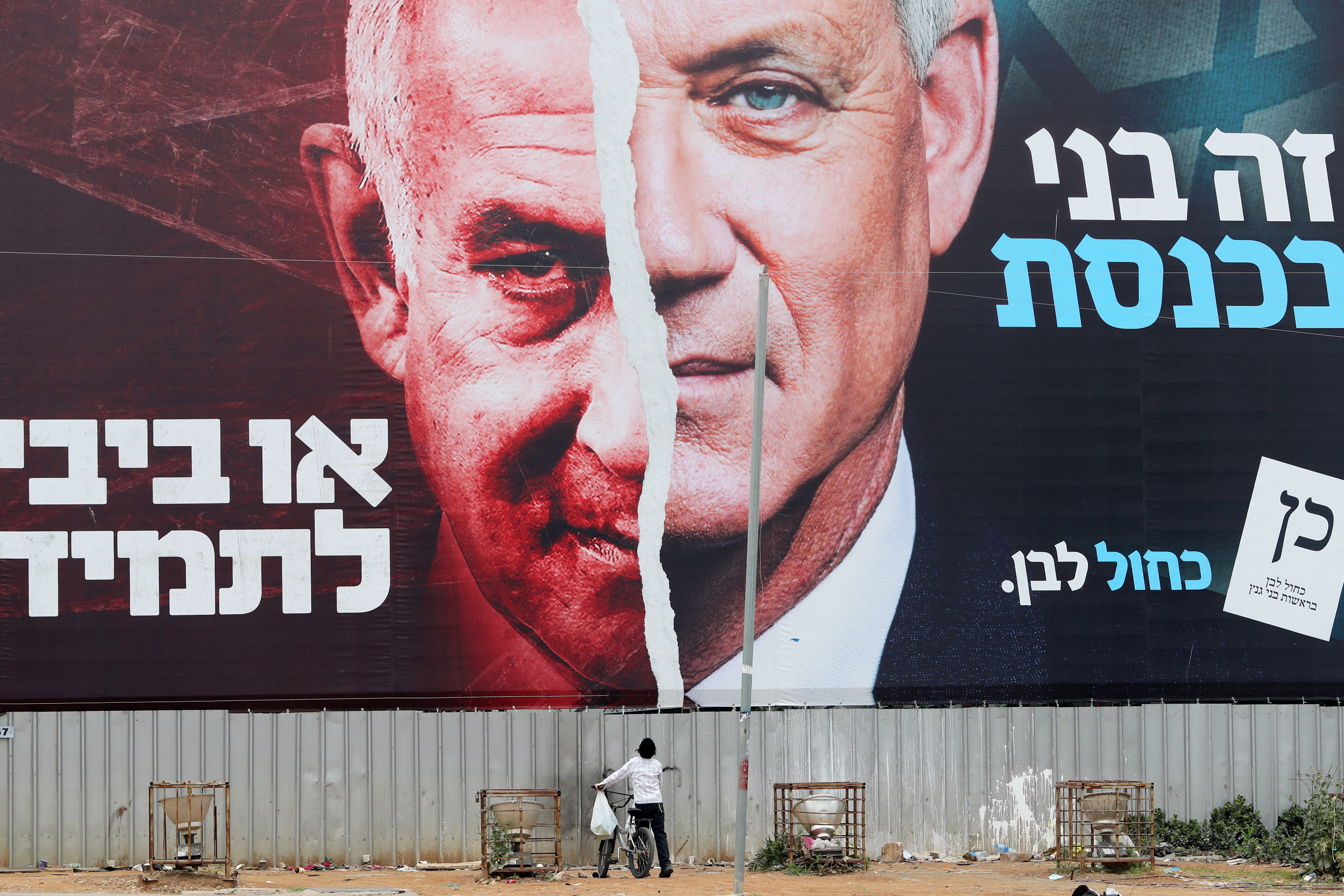 FILE PHOTO: A boy looks up at a Blue and White party election campaign banner depicting its leader, Israeli Defence Minister Benny Gantz, alongside Israeli Prime Minister Benjamin Netanyahu, ahead of the March 23 ballot, in Bnei Brak