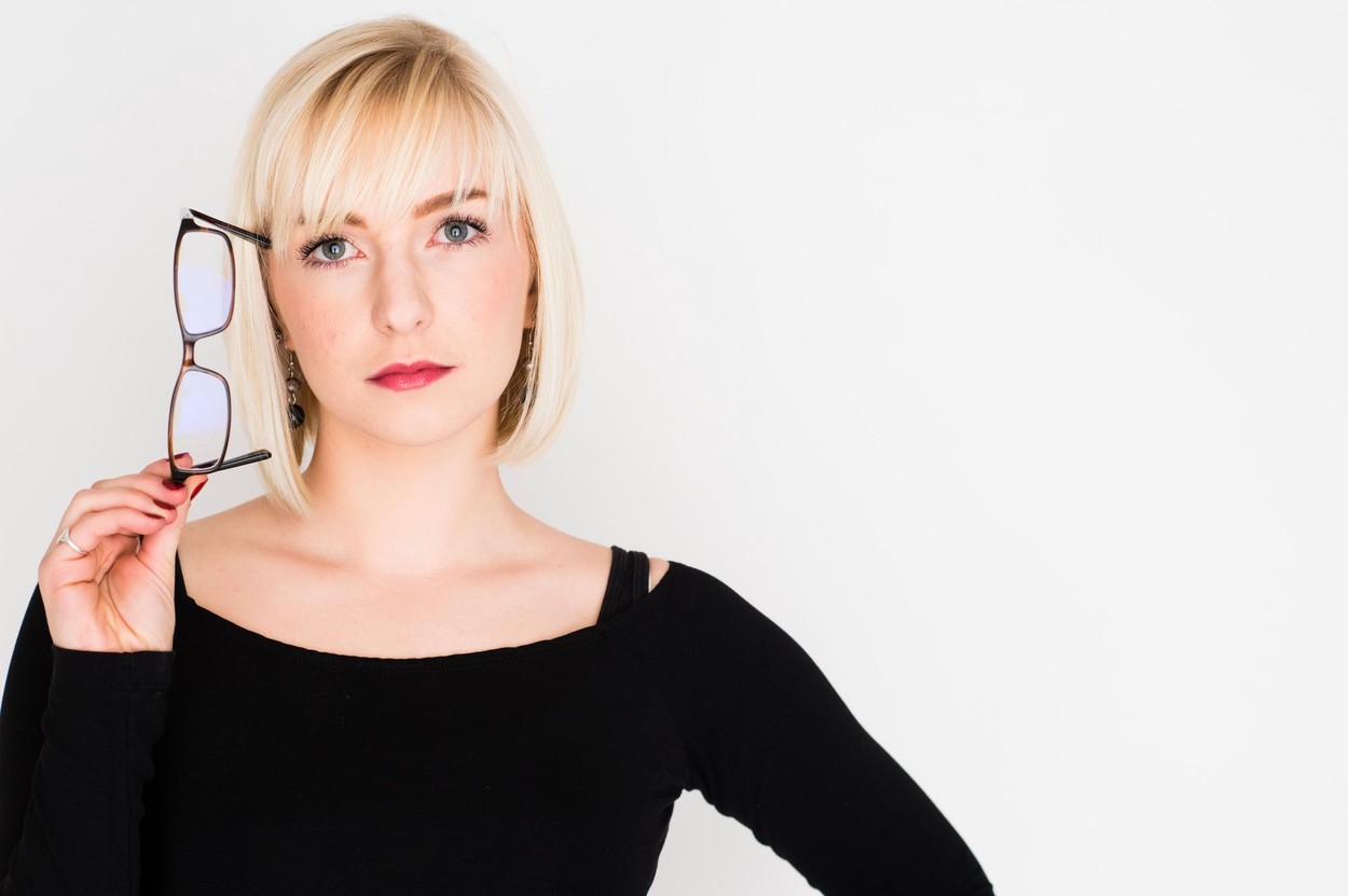 A young slim blonde blond haired woman girl, thinking, pondering, thoughtful, holding her glasses to her head UK intellectual academic clever intelligent UK