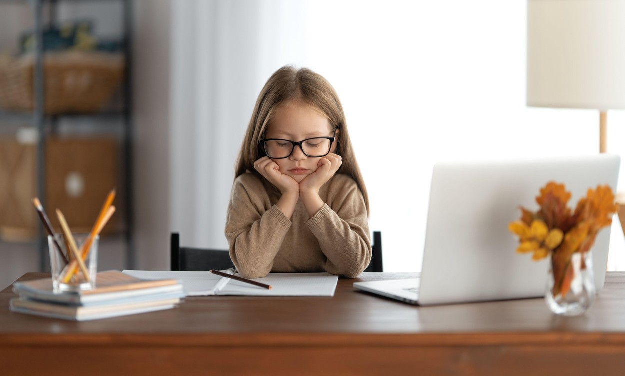 Back to school. Thinking child is sitting at desk. Girl doing homework or online education.