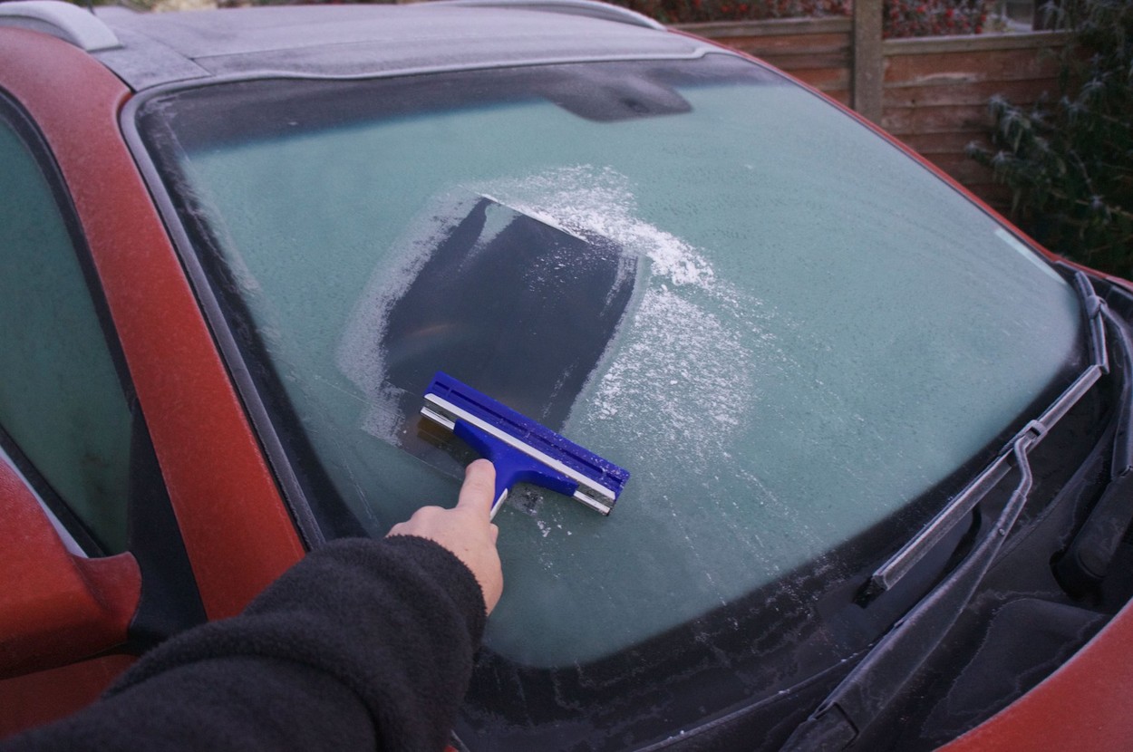Scraping the ice from a car windscreen UK winter early morning chore