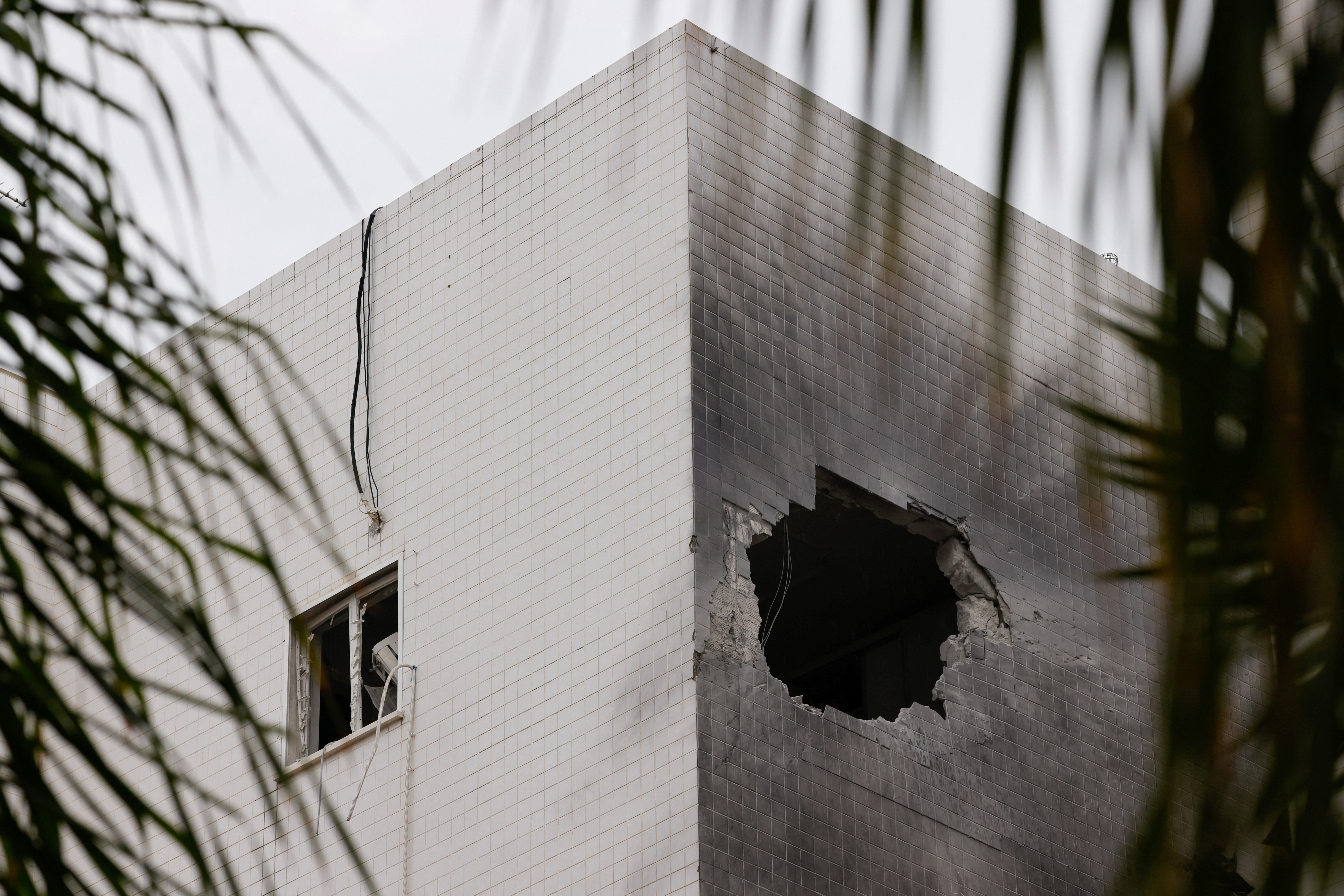 People stand next to a building which was hit by a rocket fired from Gaza, in Ashkelon