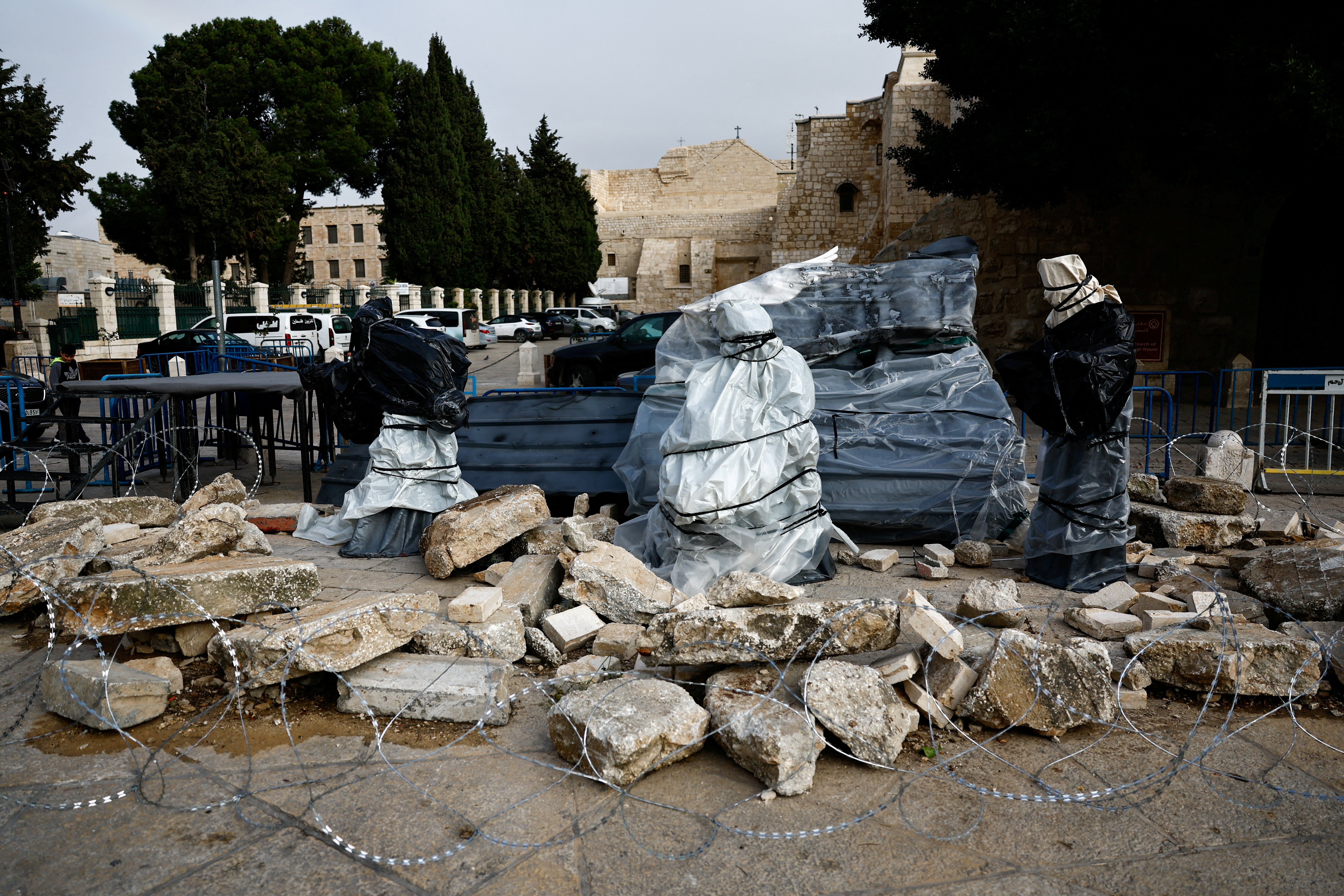 Christmas installation of a grotto with covered figures standing amid rubble, is displayed on Manger Square in Bethlehem