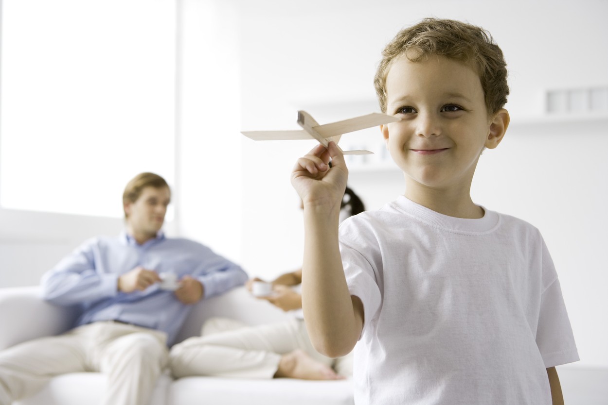Boy playing with toy airplane, parents sitting on couch in background