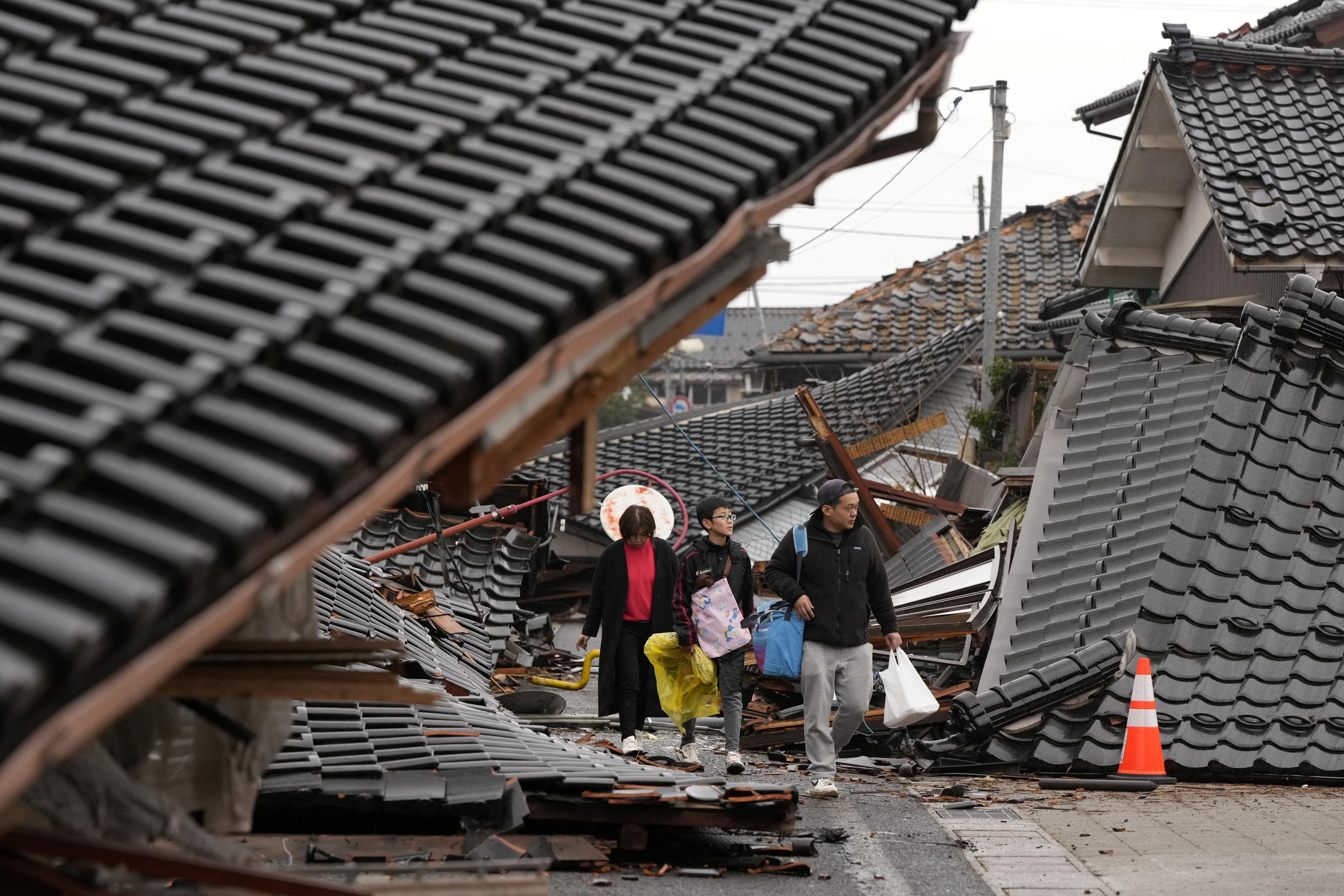 Local residents walk between collapsed houses at a tsunami-devastated residential area in Suzu