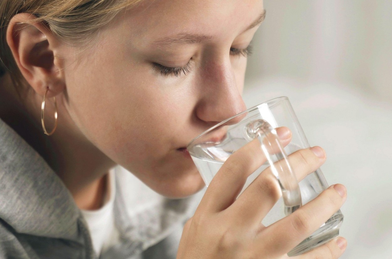 The girl drinks water from a transparent glass cup.