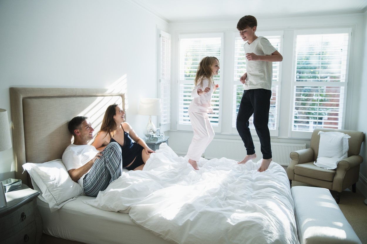 Parents watching children jumping on bed