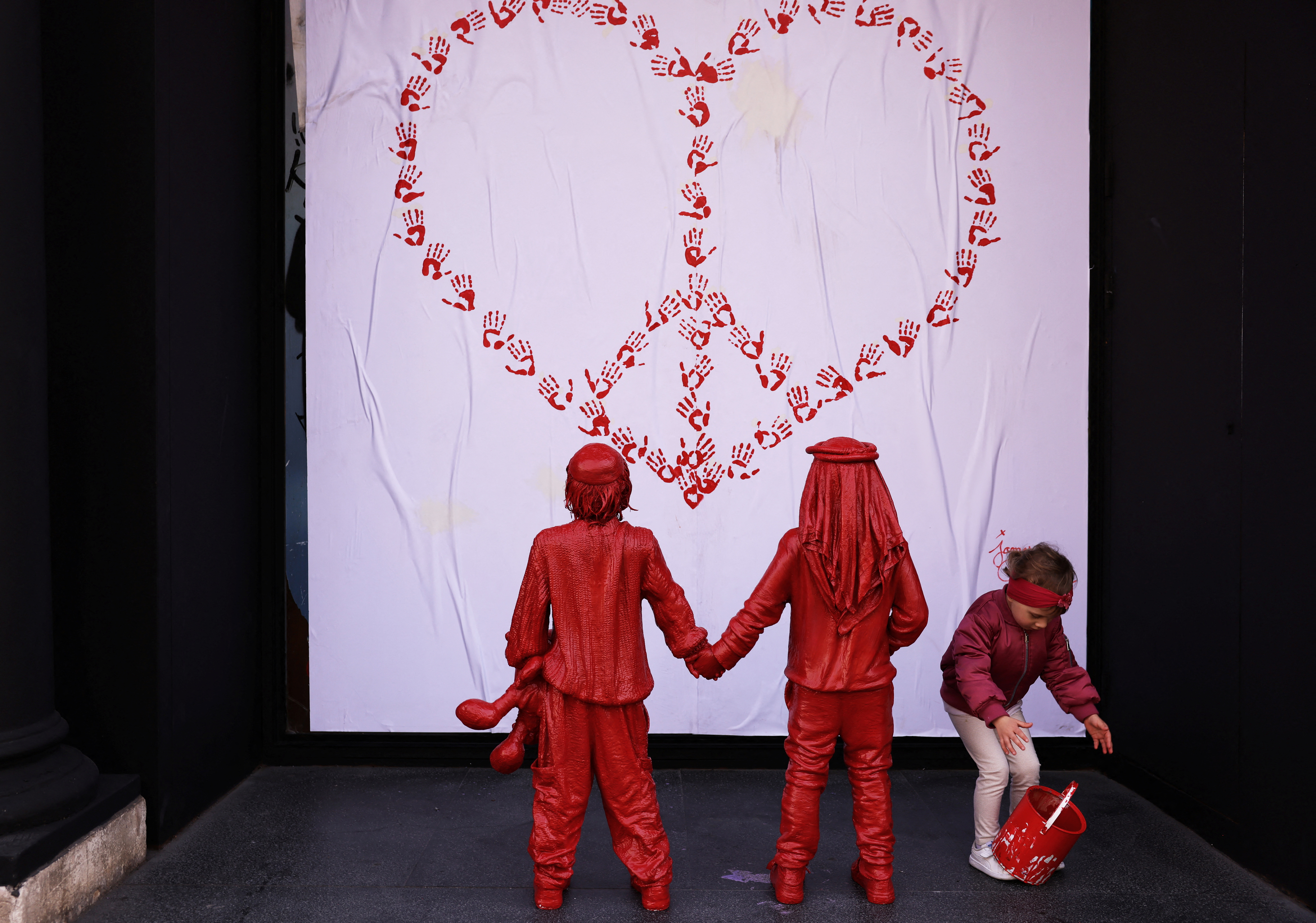 Olivia, 3, from Poland, plays with a paint can next to life-size statues of an installation entitled "Children of Peace", in Barcelona