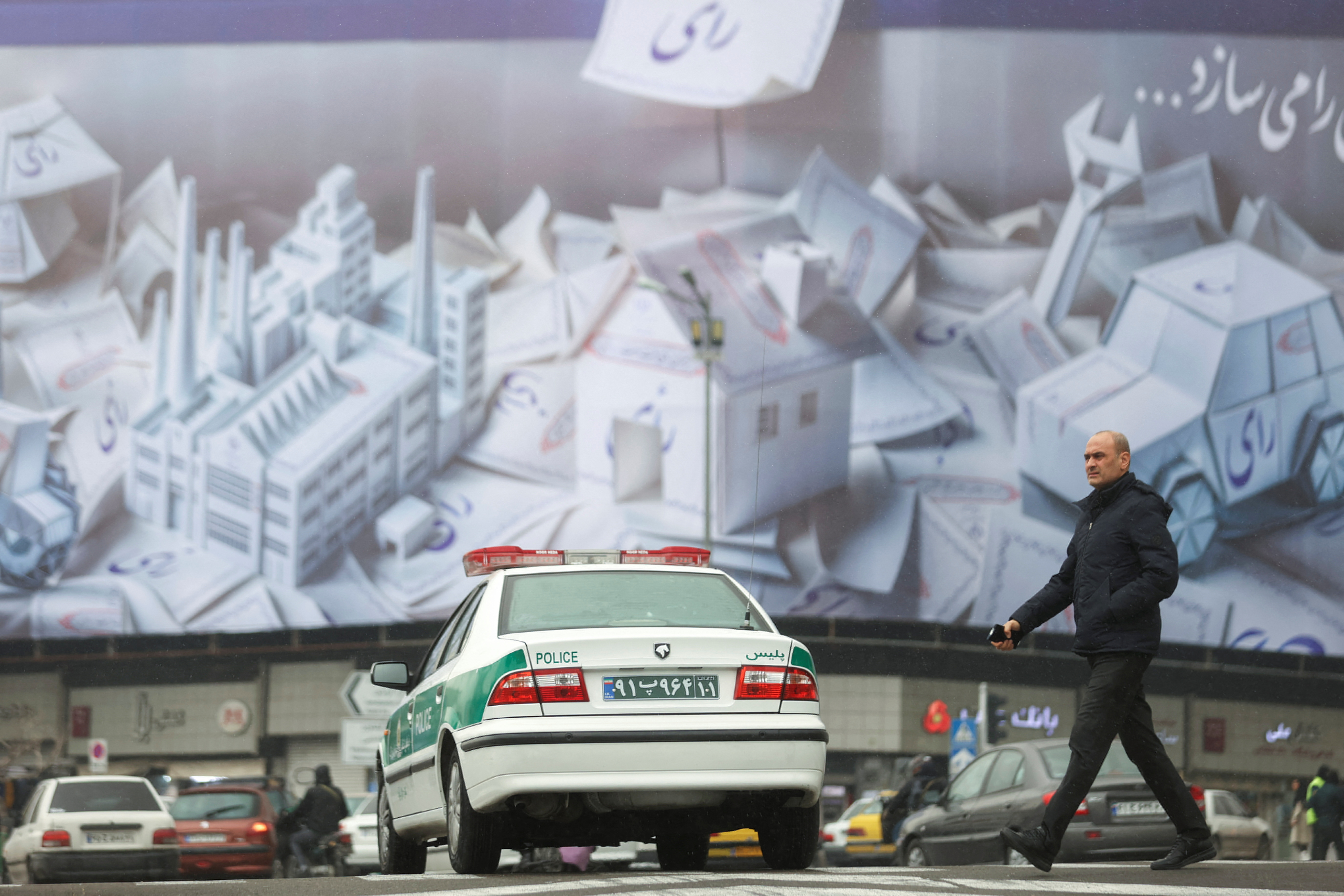 An Iranian man walks past a campaign banner for the parliamentary election during the last day of election campaigning in Tehran