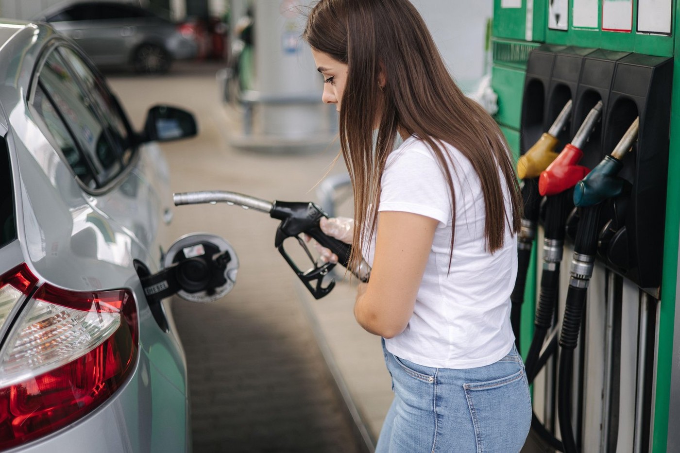Attractive young woman refueling car at gas station. Female filling diesel at gasoline fuel in car using a fuel nozzle. Petrol concept. Side view