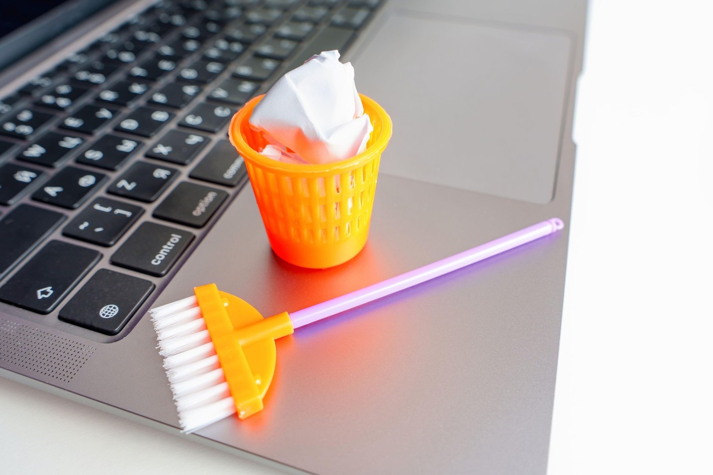 Creative computer dust and debris cleaning concept: Toy mop and trash can with paper balls placed on a laptop.