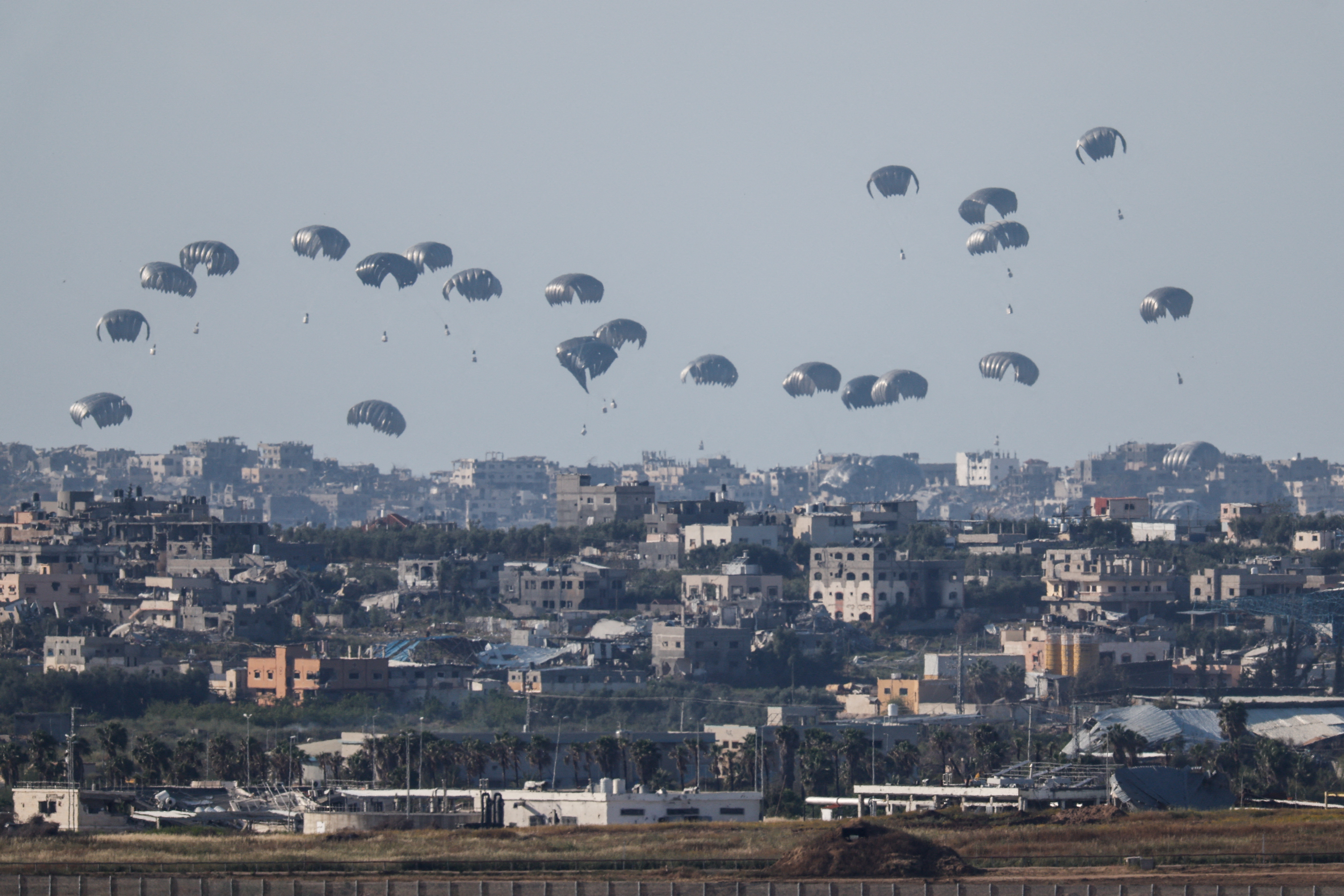Humanitarian aid falls through the sky towards the Gaza Strip, as seen from Israel