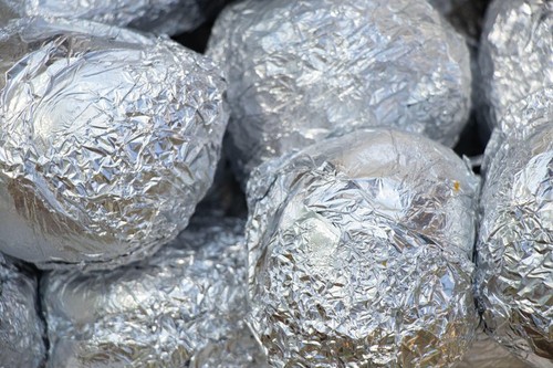 Bake potatoes in foil on the grill in the coals in the summer at a picnic, food on the grill