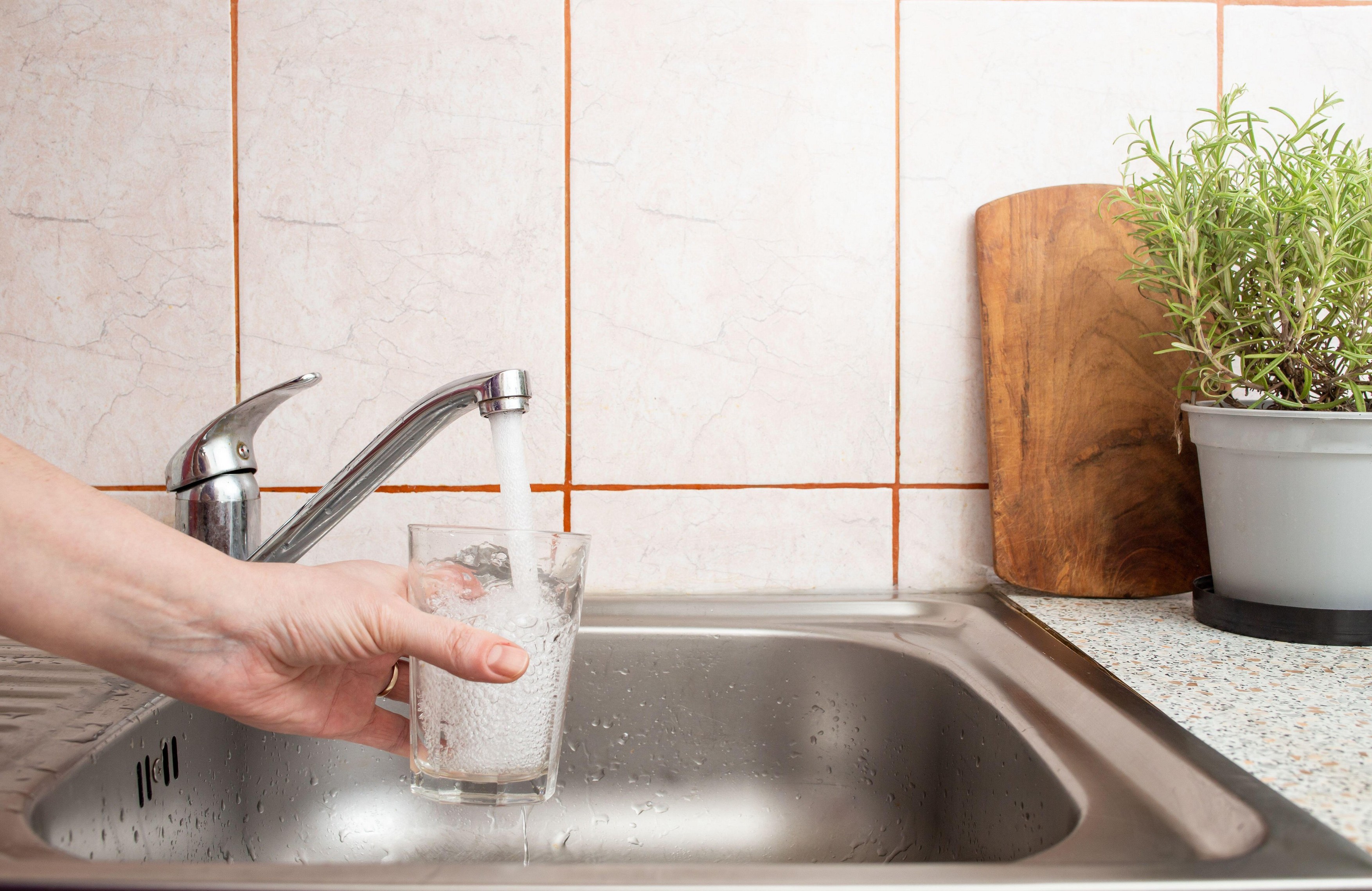 Woman hand holding a clear glass under a stream of fresh tap water from a kitchen sink faucet , soft focus