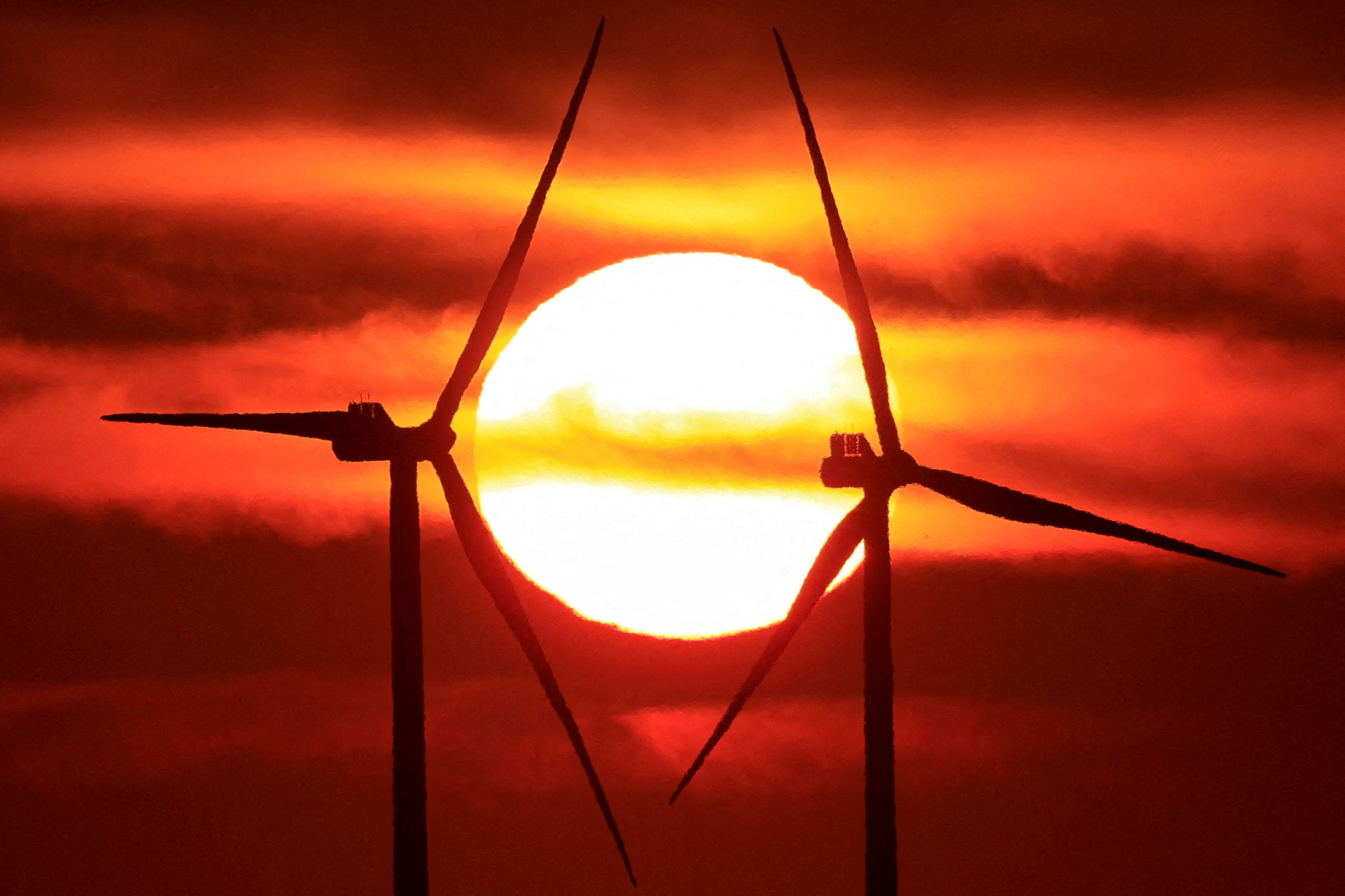 FILE PHOTO: Power-generating windmill turbines and electricity pylons are pictured during sunrise at a wind park in Avesnes-le-Sec