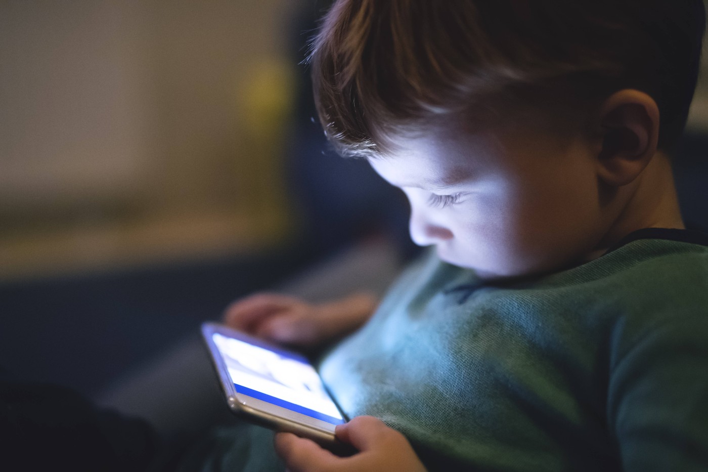 Cute boy sitting on bed watching something on smartphone. Children s screen time. Cute boy toddler sitting on bed and wa