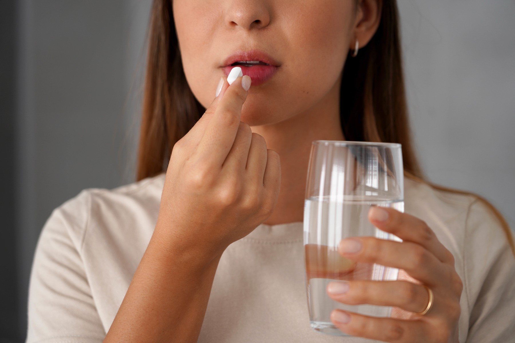 Young woman takes a pill while holding a glass of water in her h