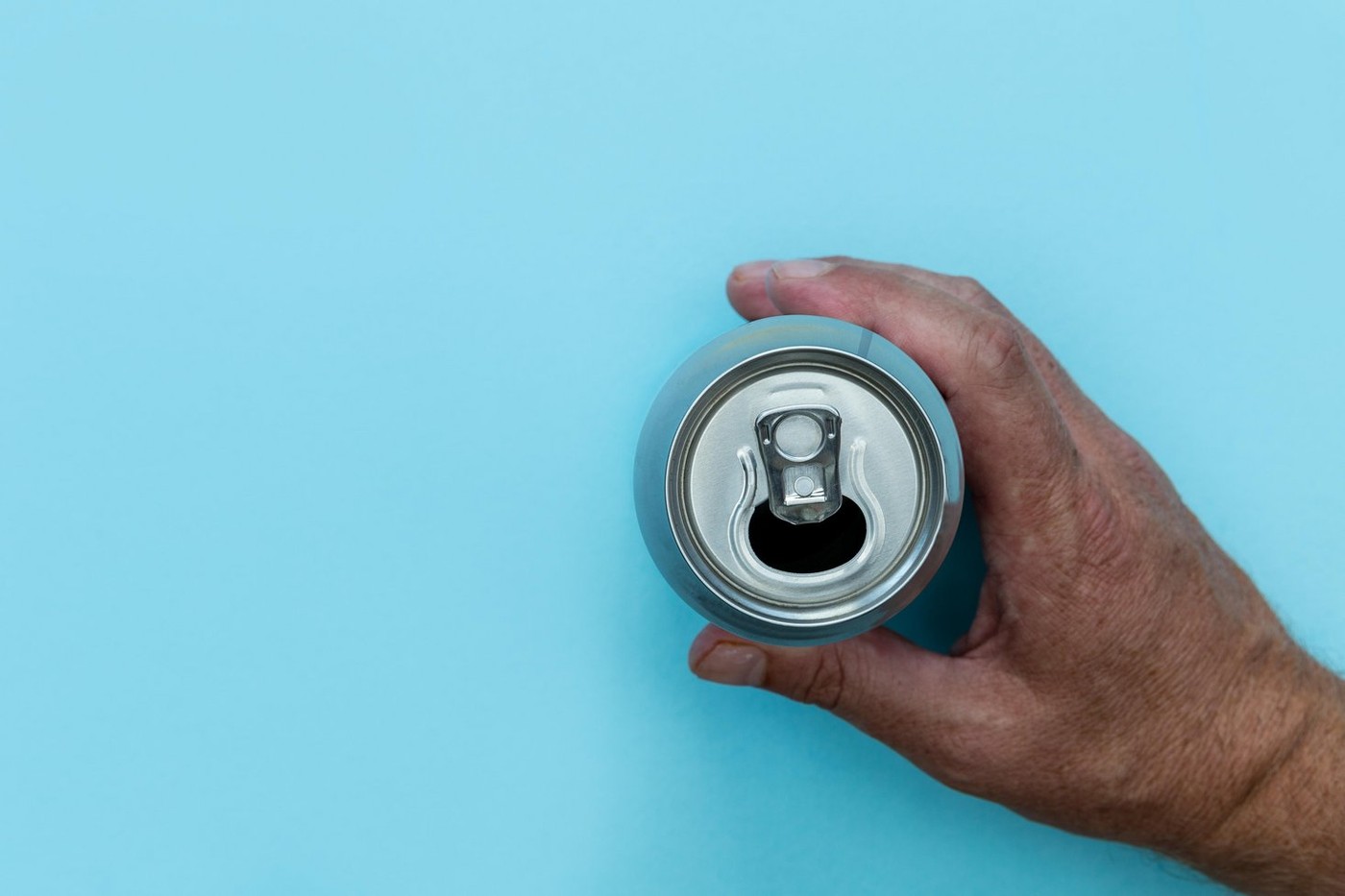Hand holding drinks can on bright blue background