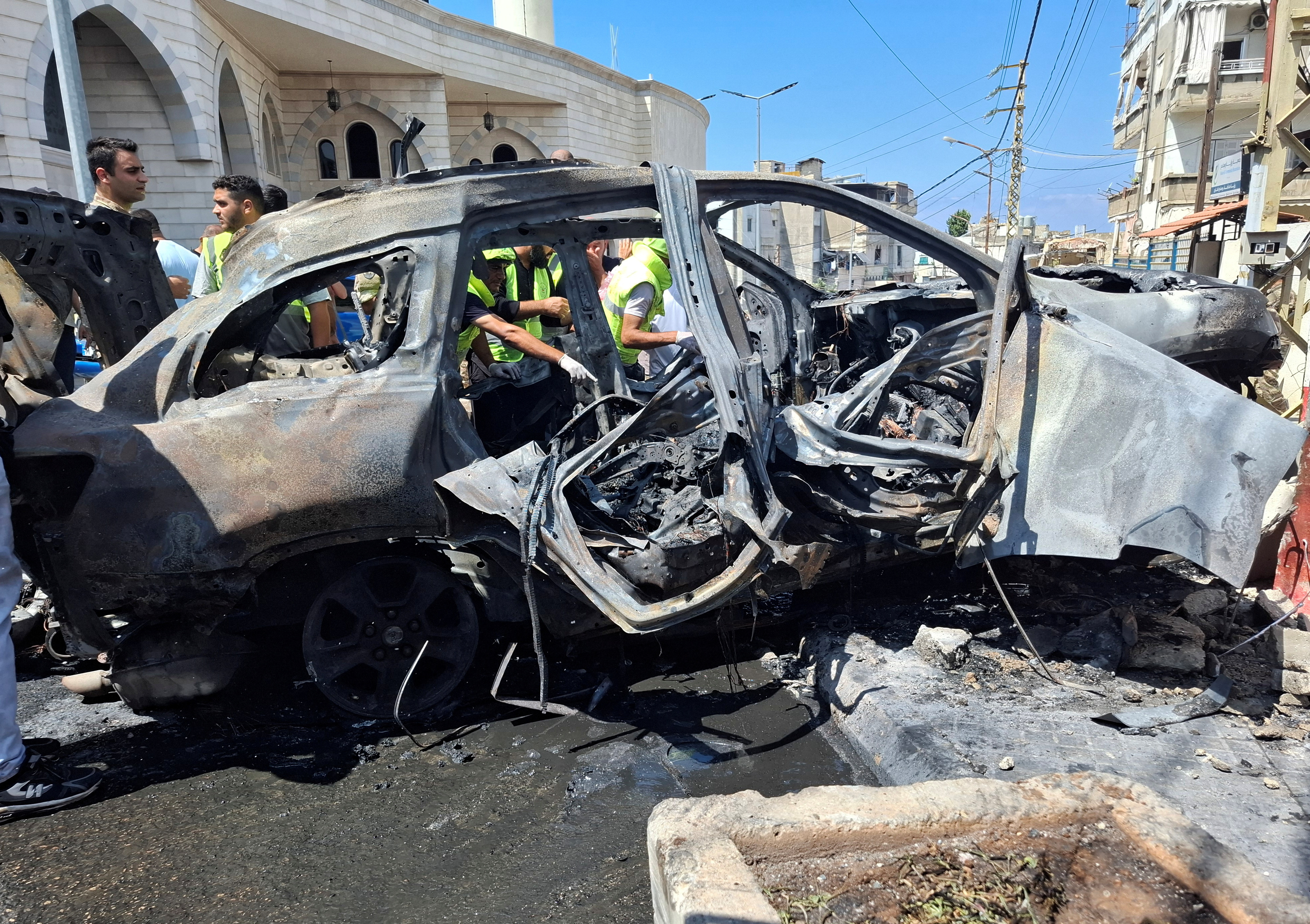 People and Lebanese army members stand near a burnt car after an Israeli strike on the outskirts of the southern port city of Sidon according to two Palestinian sources