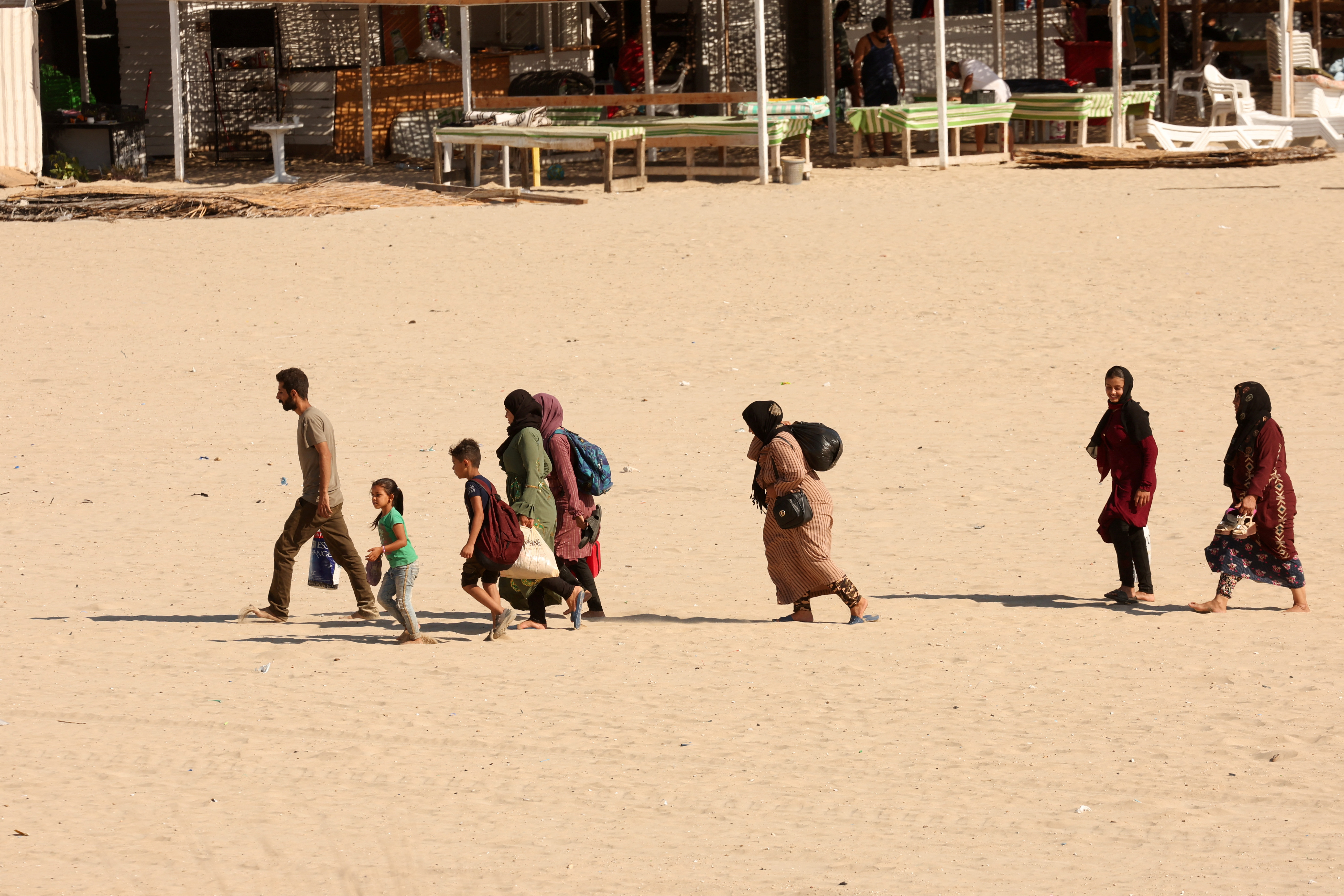 People carry belongings at a beach as they flee, in Tyre