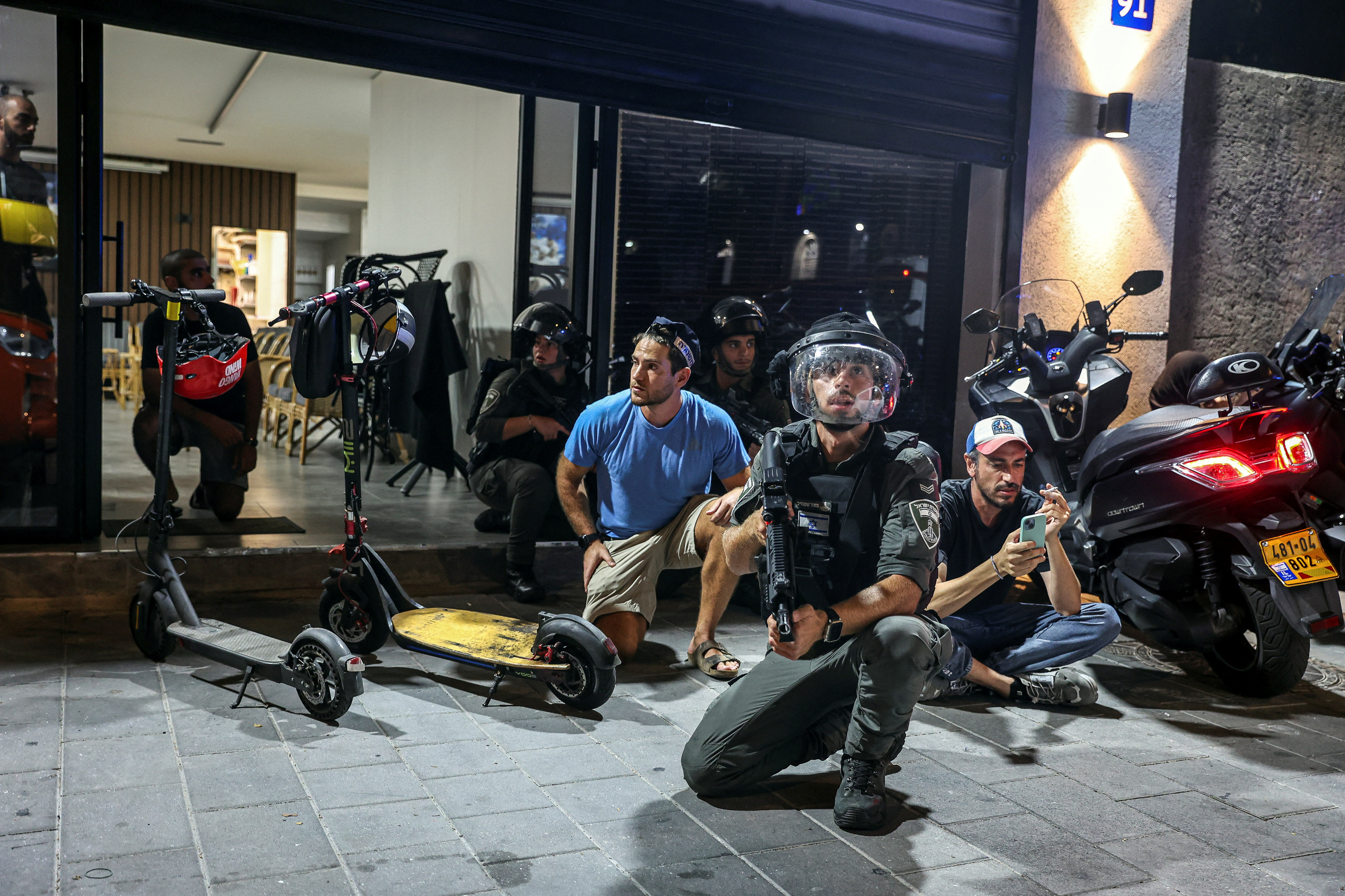 Israeli police and border police take cover during sirens, after Iran fired a salvo of ballistic missiles at Israel, and near the site of a fatal shooting attack in Jaffa