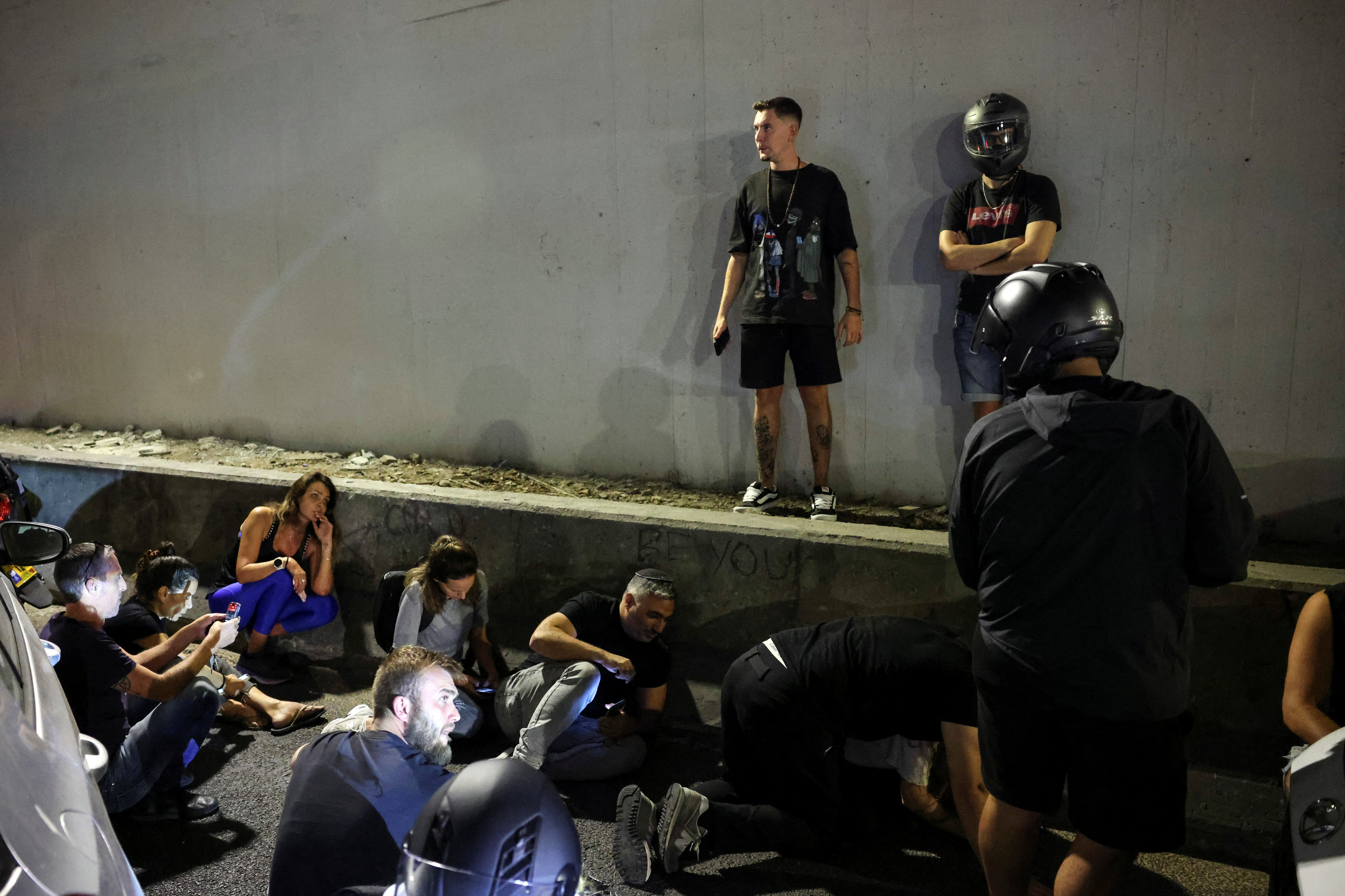 People take cover by the side of a road as a siren sounds and after Iran fired a salvo of ballistic missiles at Israel, in Tel Aviv