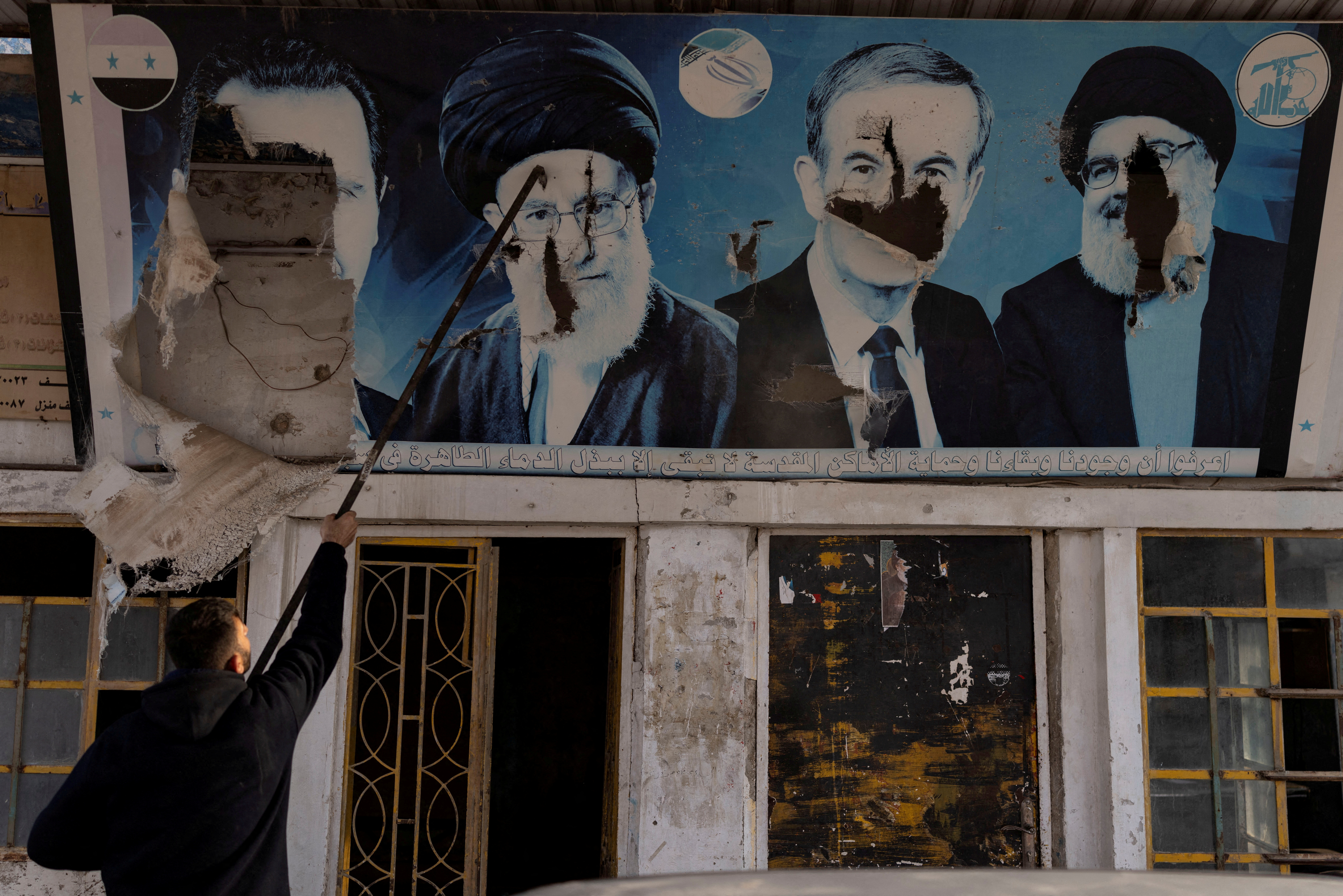 FILE PHOTO: A gas station worker tears down pictures at a gas station in Nubl in rural Aleppo
