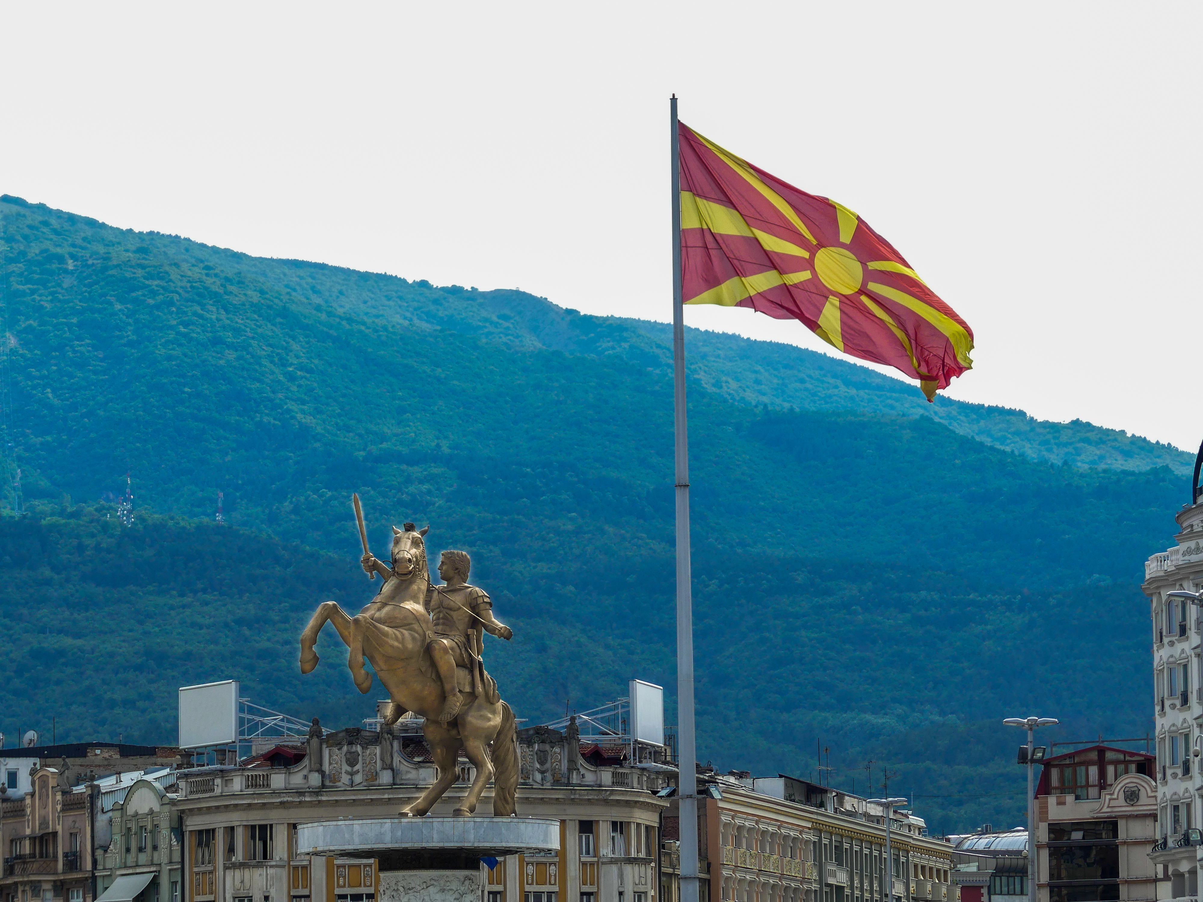 Macedonian,Flag,With,Skopje's,Landmark,Statue,In,Background.