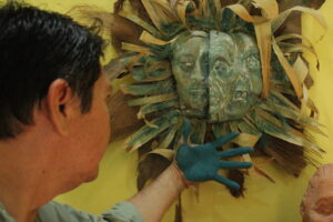 1737119882-Luis-May-Ku-49-admires-a-three-sided-facemask-he-sculptured-adorned-with-dried-palm-leaves-and-painted-in-Maya-Blue-inside-his-home-in-Dzan-Yucatan-Mexico-on-9-September-2024-300x200.jpg